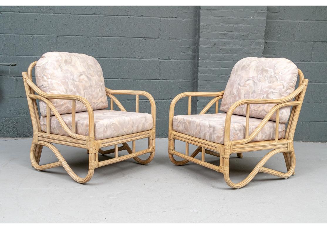 A very well-crafted Pair of vintage rattan lounge chairs with a sweeping arm style that flows simultaneously into the rounded back of the chair and forms scrolling legs at the base. The backrest with vertical supports and the seat constructed with
