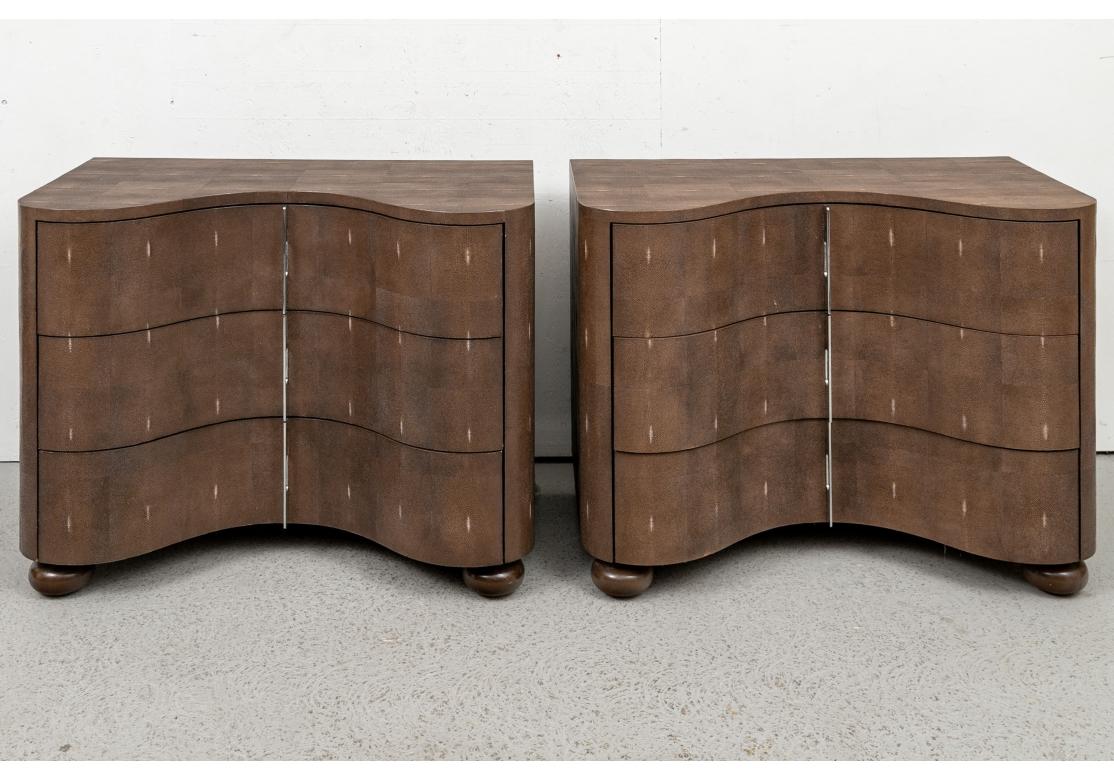 A sophisticated and striking pair of serpentine chests. The pair of chests in brown faux shagreen with shaped serpentine cases in front. The three long drawers with matching vertical chrome pulls. Raised on complimentary painted bun feet. 
Measures:
