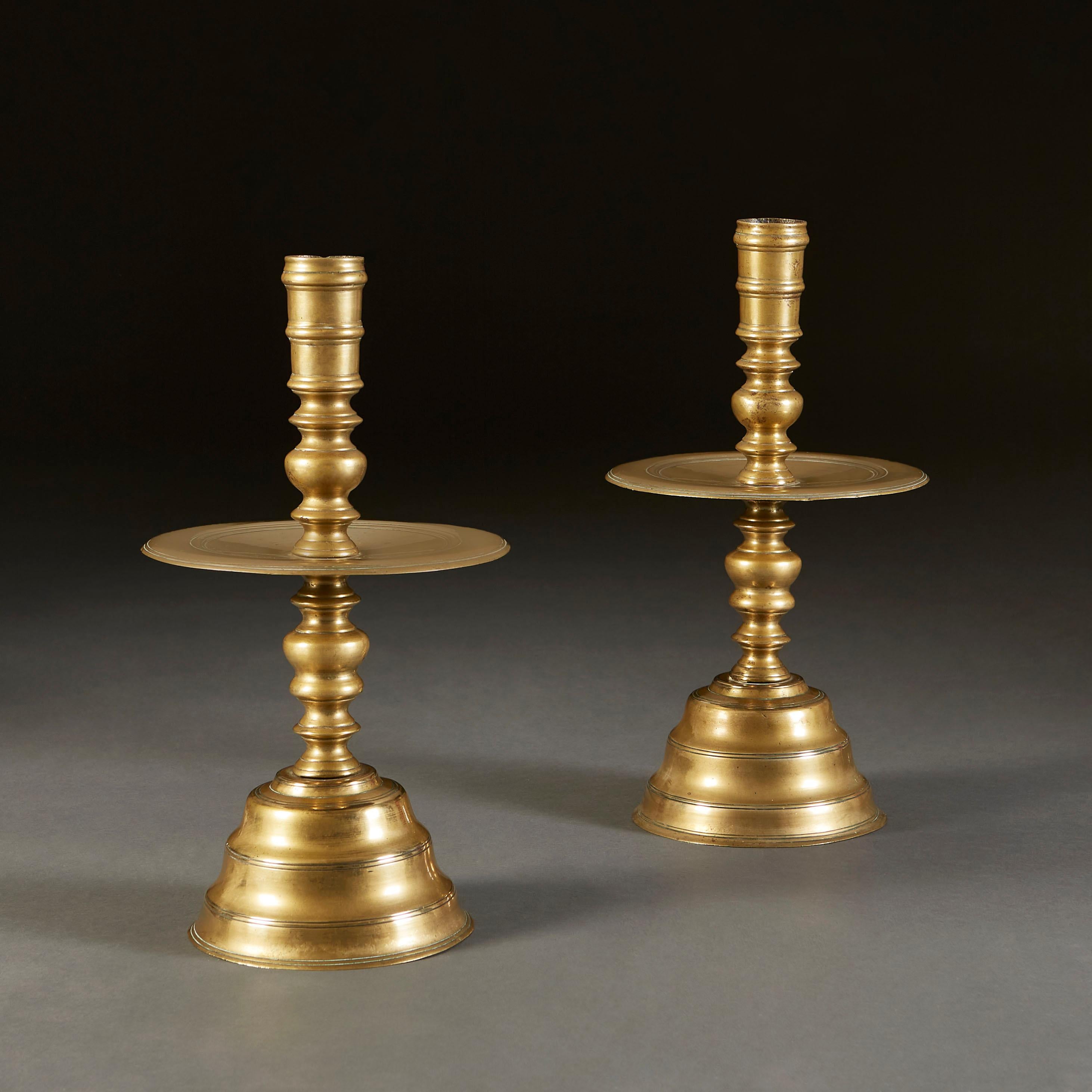 A fine pair of seventeenth century Dutch brass candlesticks, with molded baluster turnings to the column. The candlesticks feature mid mounted drip trays between knopped stem details, atop a stepped base.