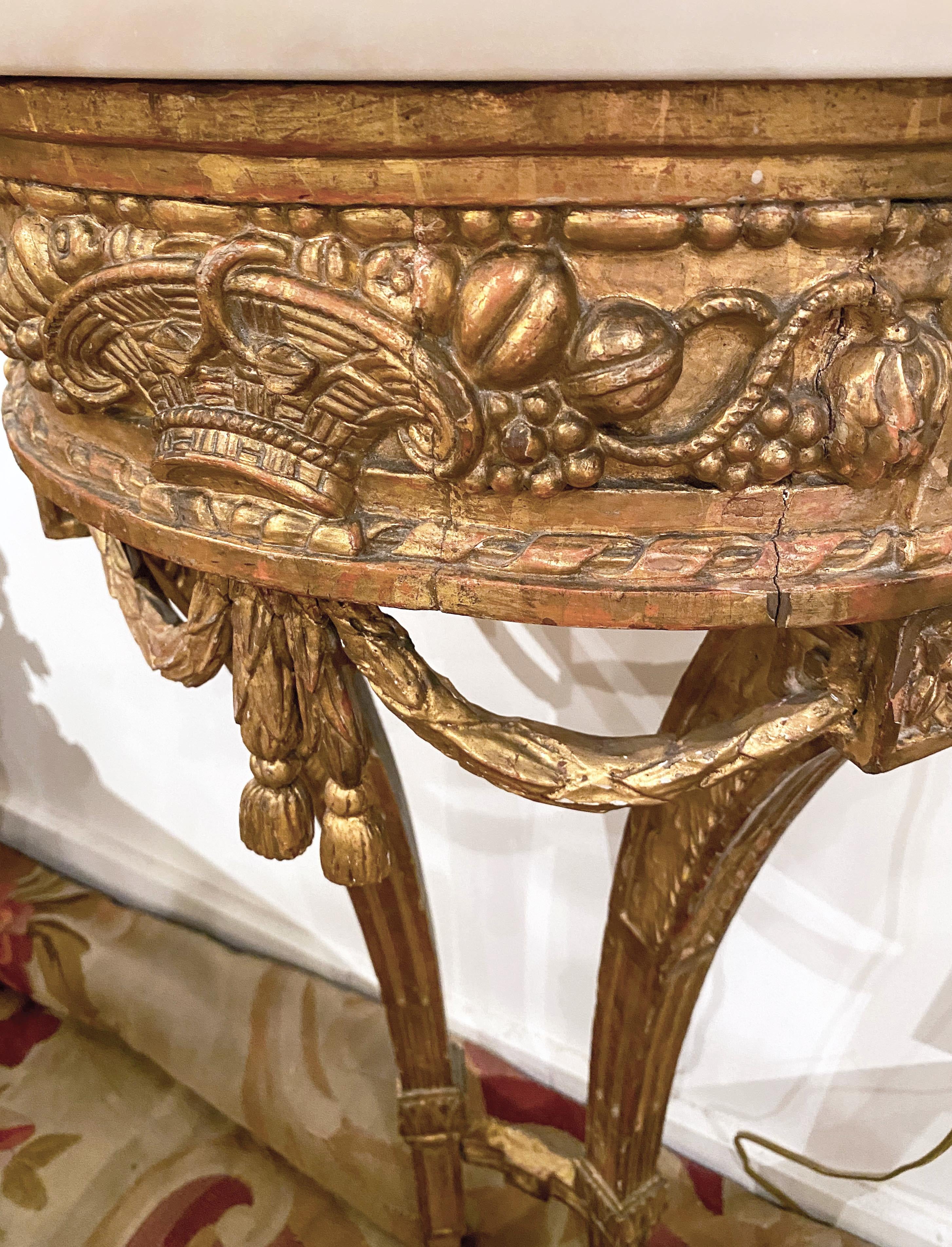 A fine pair of petite Louis XVI. 
Carved giltwood console tables,
18th century.

Each with a D-shape white marble top above the guilloche-carved frieze, centered by a woven basket flanked by fruit, above laurel swags, raised on incurved fluted legs,