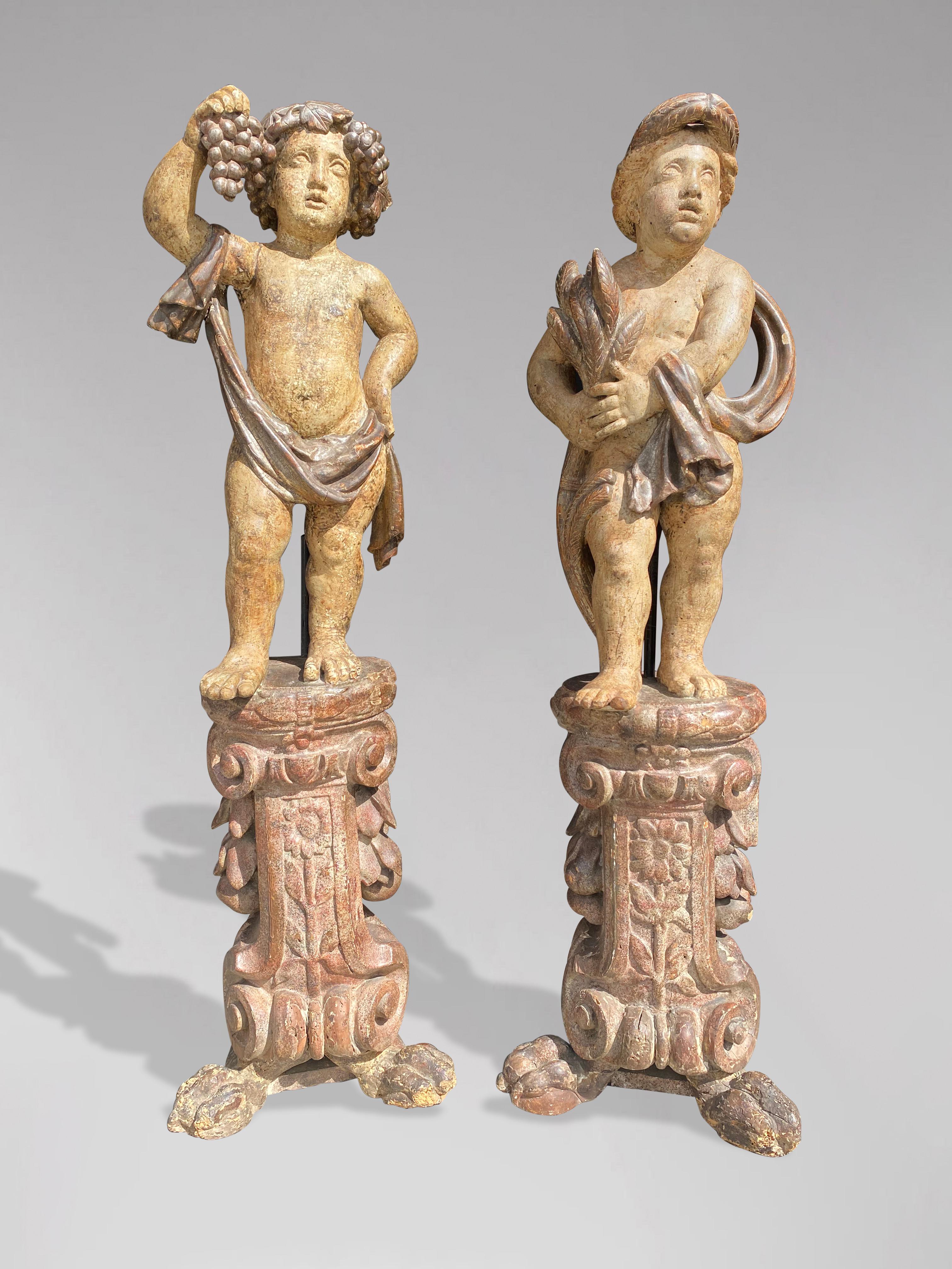 A fine pair of 18th century tall Italian carved wood harvest cherub sculptures. These sculptures each hold a piece of harvest aloft their curled heads, forms elegantly poised as if caught in a musical performance. A close eye will additionally