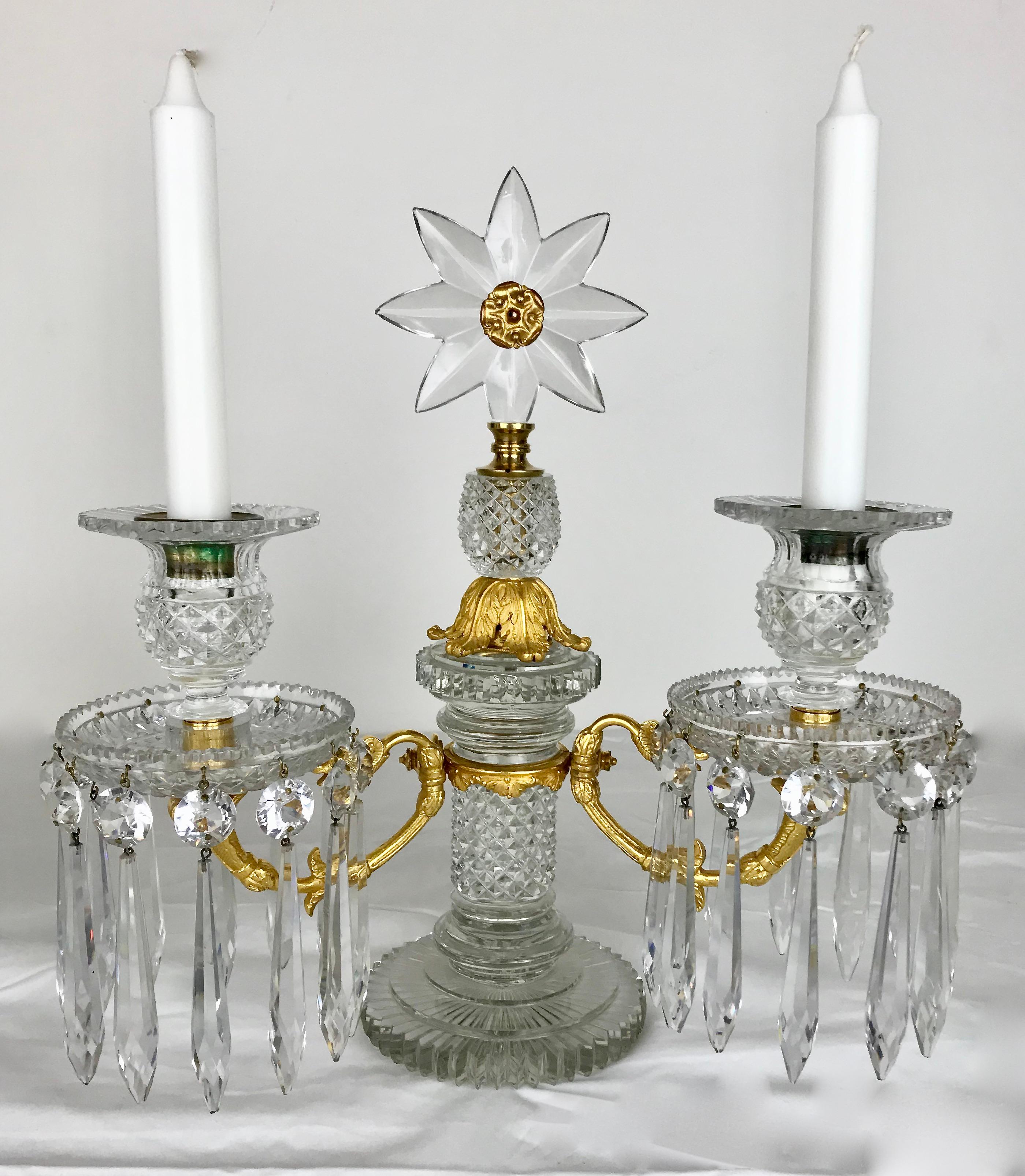 Cette exquise paire de candélabres Regency à deux lumières est attribuée au célèbre fabricant Apsley Pellatt. Les bases circulaires à gradins avec des colonnes taillées en diamant soutiennent des bras jumeaux en bronze doré. Les fleurons en forme