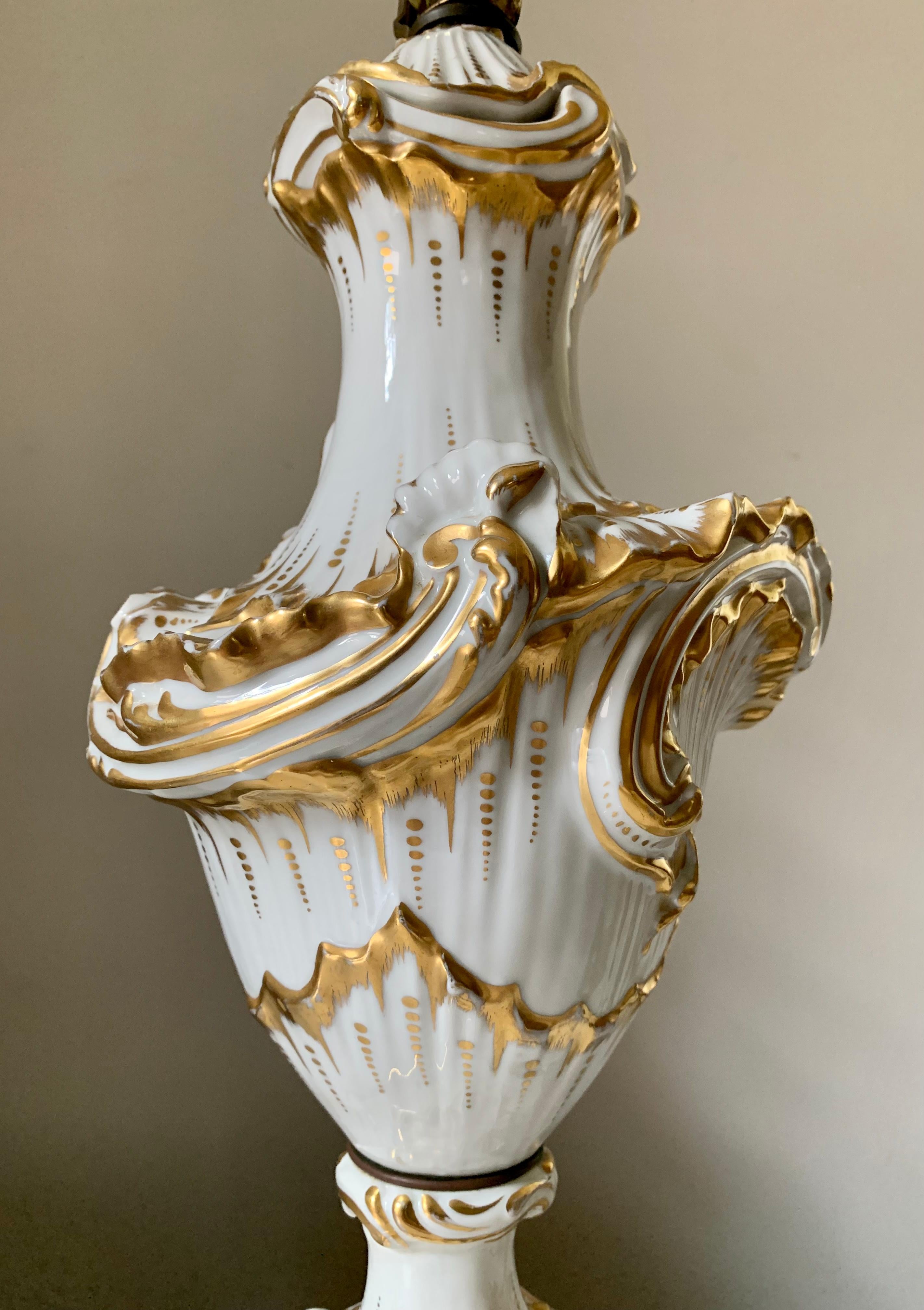 Luminous white and gold porcelain table lamps in the Rococo/ Louis XV style, mounted on Carrara marble bases. Wave upon wave of rocaille decoration highlighted in gold, formerly a pair of covered vases converted into lamps. Fine quality