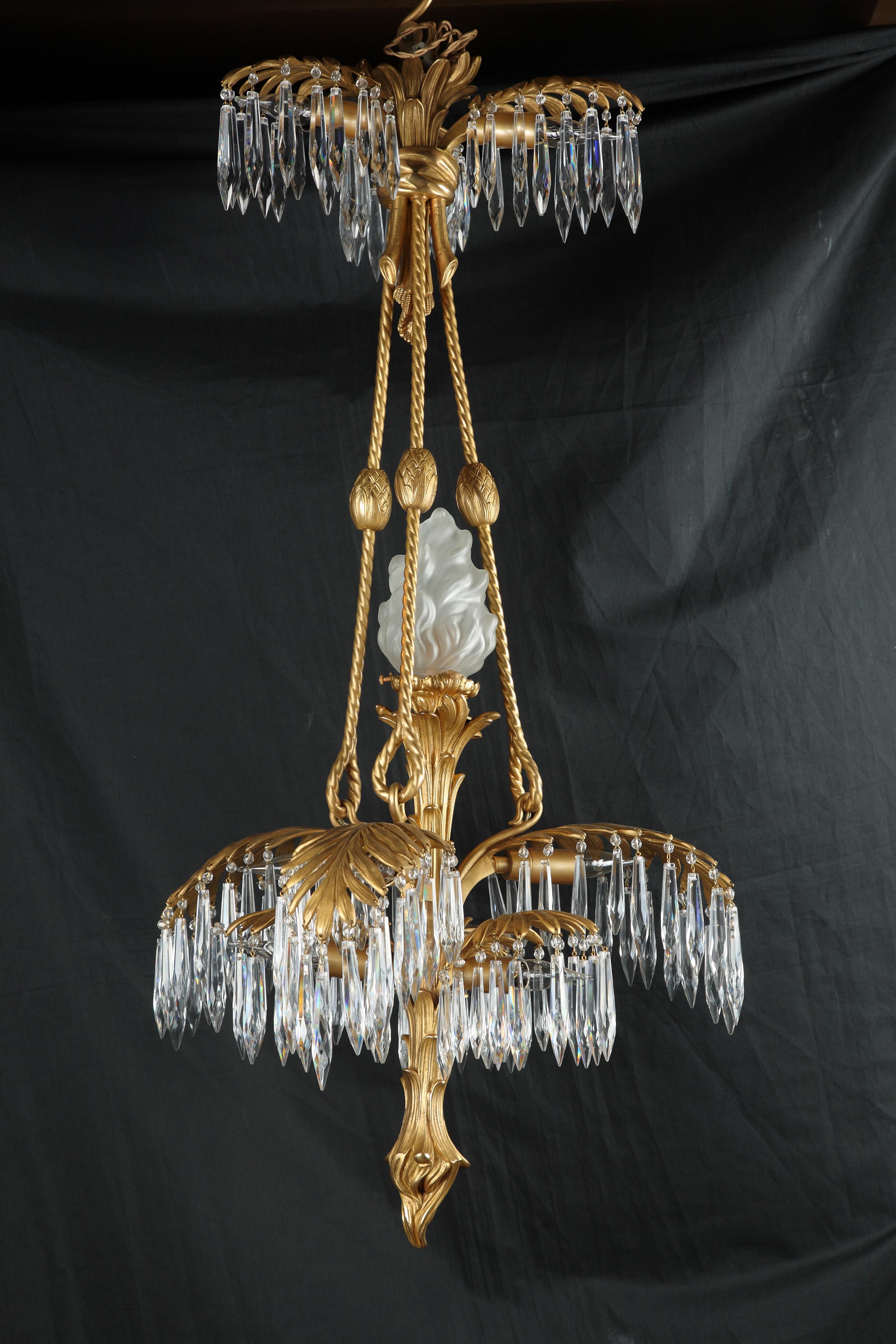 Superb gilt bronze chandelier with a palm tree shaped shaft issuing elegant leaves from which hang cut-crystal pendants and hiding nine lights on three levels connected by twisted cords. A tenth-shaped torch light adorns the center of the