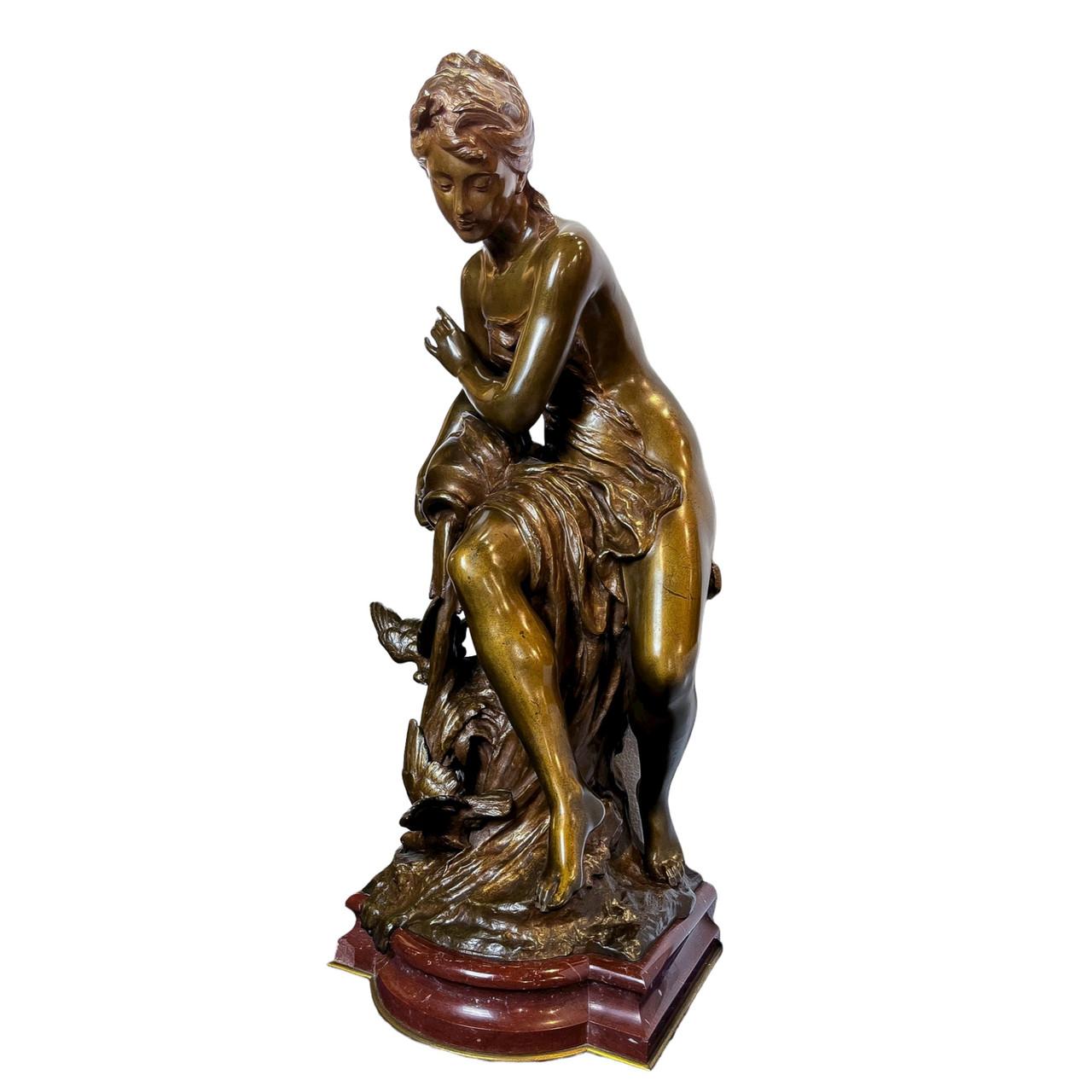 A beauty sits on a stone, pouring water from a jug onto the rock beside her. Two birds play in the water as it cascades down. The woman wears a wreath around her head with a piece of fabric to protect her modesty. The statue sits on rouge marble