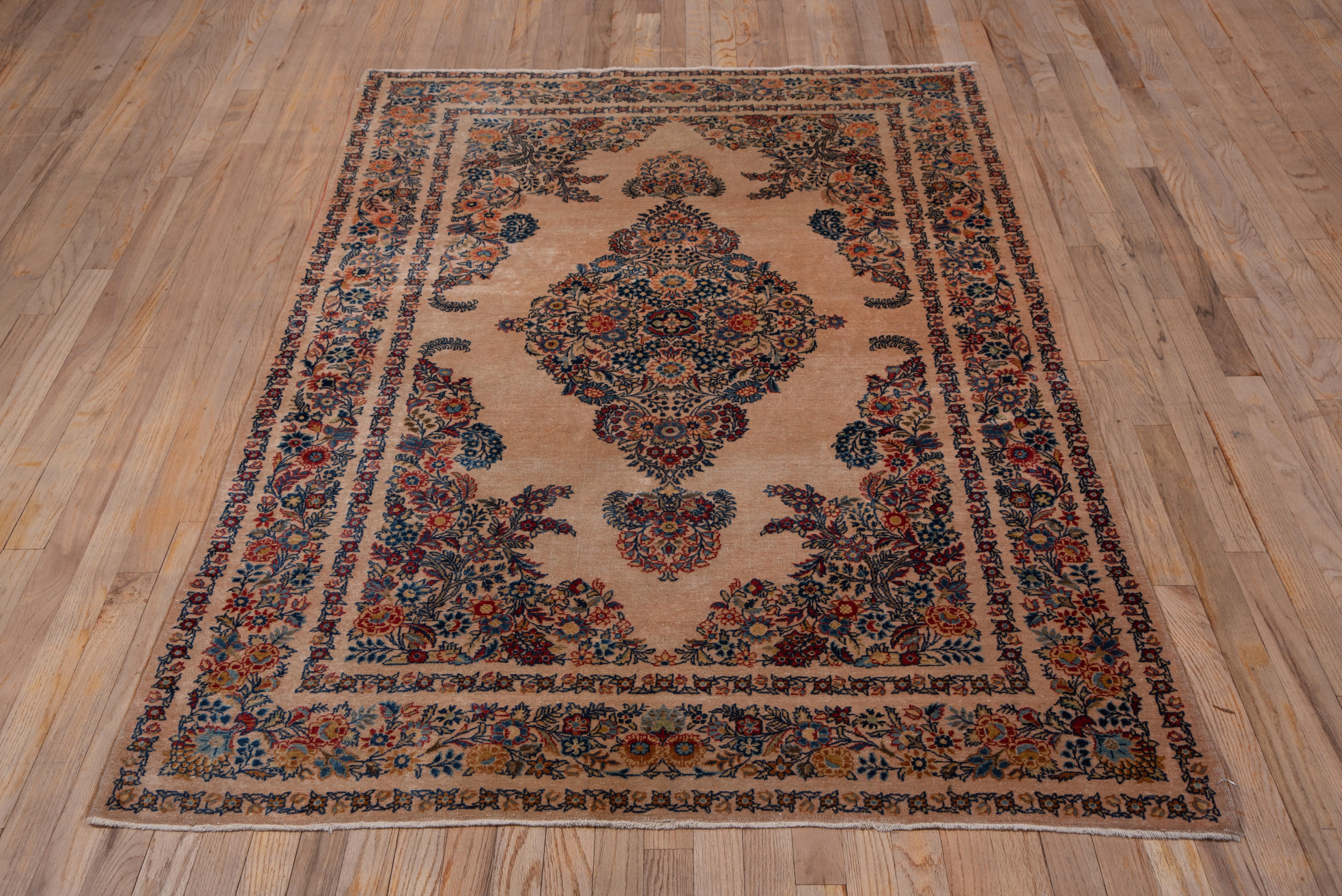 In the popular Kerman style with a side to side creamy beige open field and en suite medallion and corners composed of closely set floral sprays, this central Persian town rug has a fine weave and velvety short, erect pile. The floral borders show