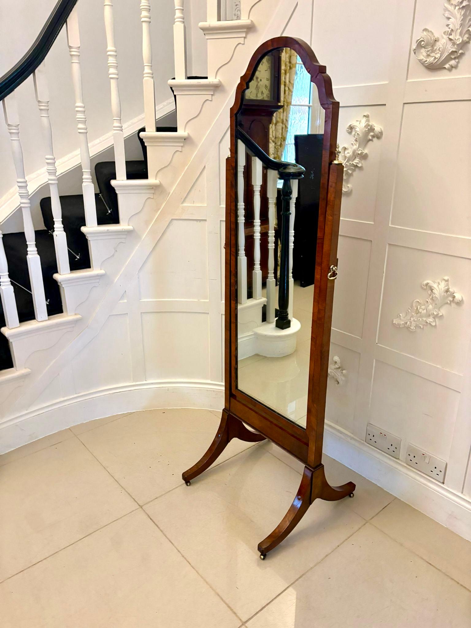 A stylish early 20th-century walnut cheval mirror. The mirror features an elegantly shaped rectangular plate set within a finely figured walnut frame supported between twin uprights with brass side adjusters and decorative finials allowing the