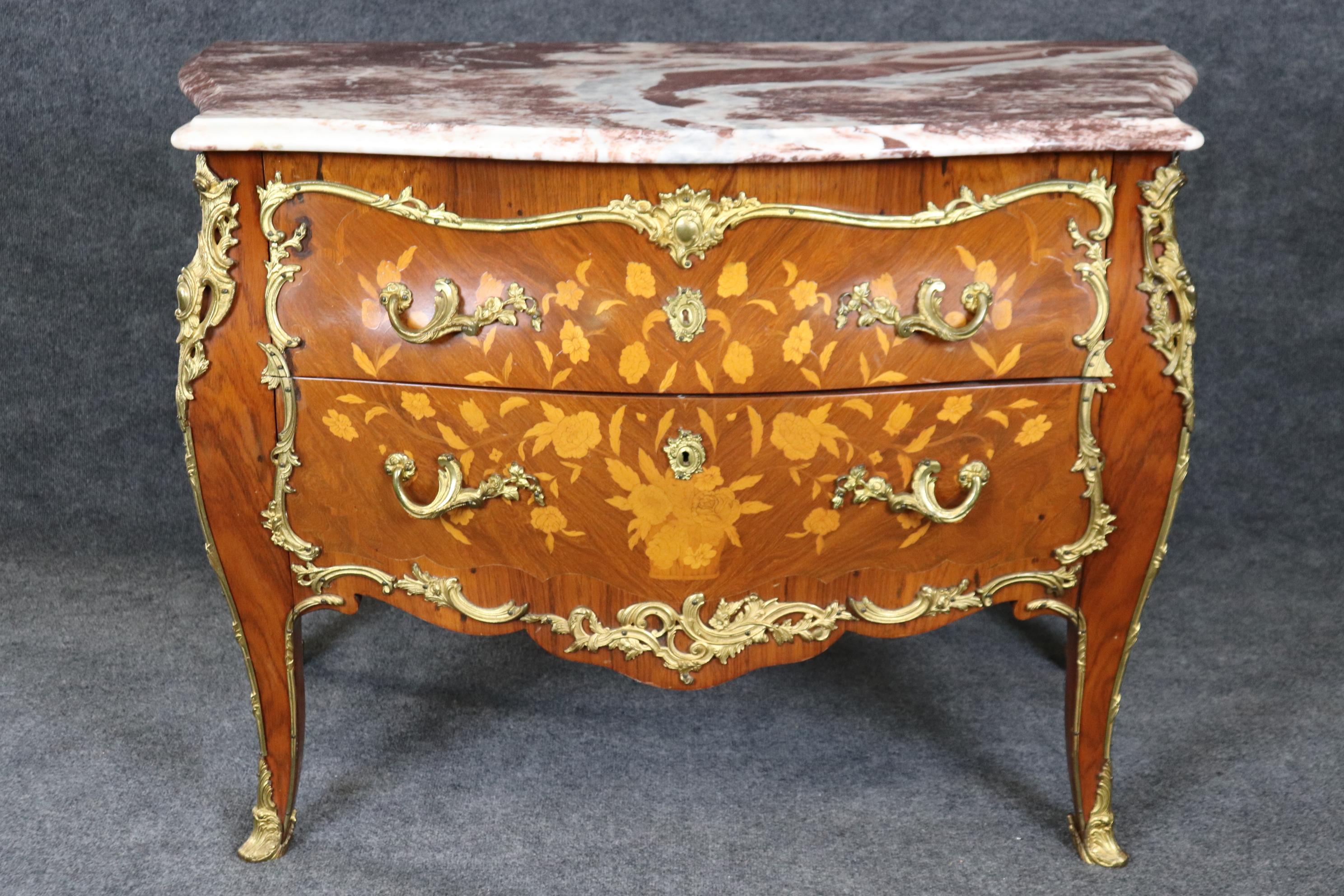 This is a truly exceptional commode. Made of the finest satinwood, walnut, and tulipwood and inlaid with sprays of flowers and a gorgeous slab of luxurious plum colored and white marble top. The commode is trimmed in superbly cast bronze ormolu and