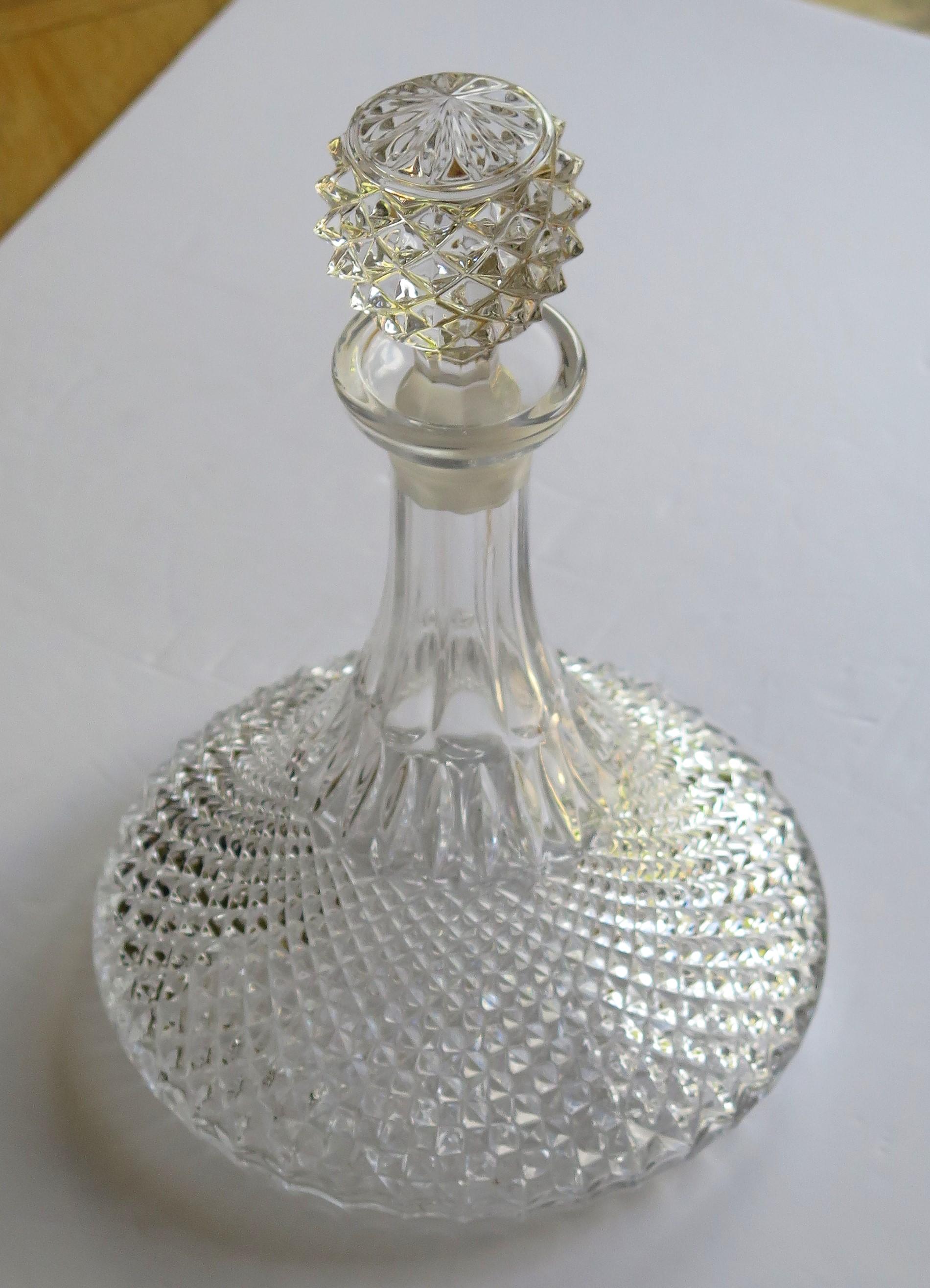 This is a high quality ship's decanter with a wide base made from heavy lead crystal or cut glass having a soft light grey color.

The decanter is diamond cut to its lower half with the diamonds graduating from the base, getting smaller towards