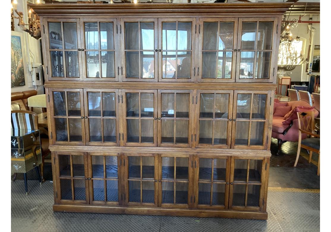 A meticulously crafted solid oak Wall Cabinet in three tiers having nine sets of double four glass pane doors with intentionally distressed brass pulls behind which is one fixed shelf. Tremendous storage and may be used in a variety of interior