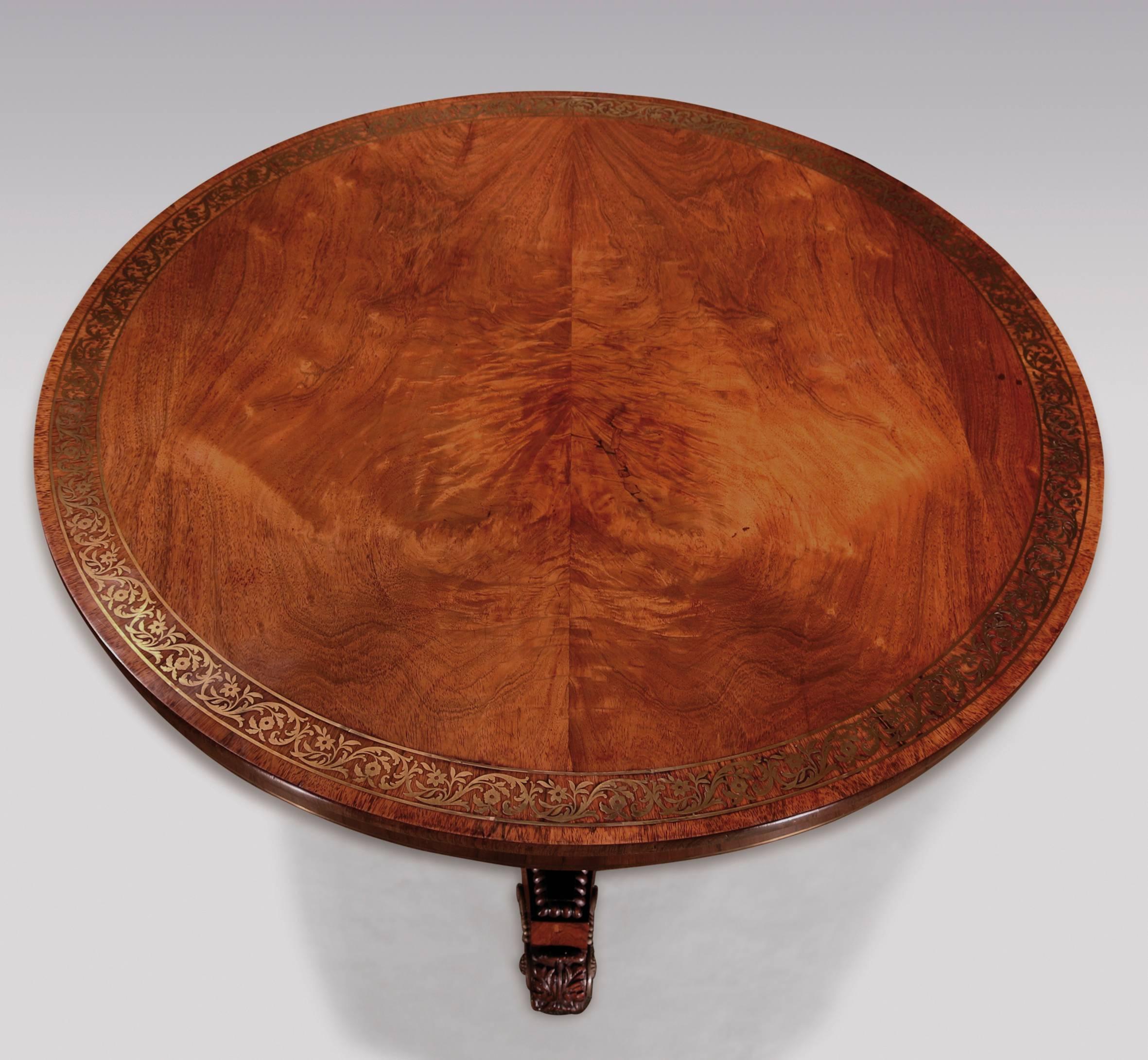A fine quality early 19th century Regency period mahogany breakfast table, having brass inlaid flame figured circular top, raised on triangular stem with brass urn inlay, supported on leaf carved and beaded concave platform base, ending on acanthus