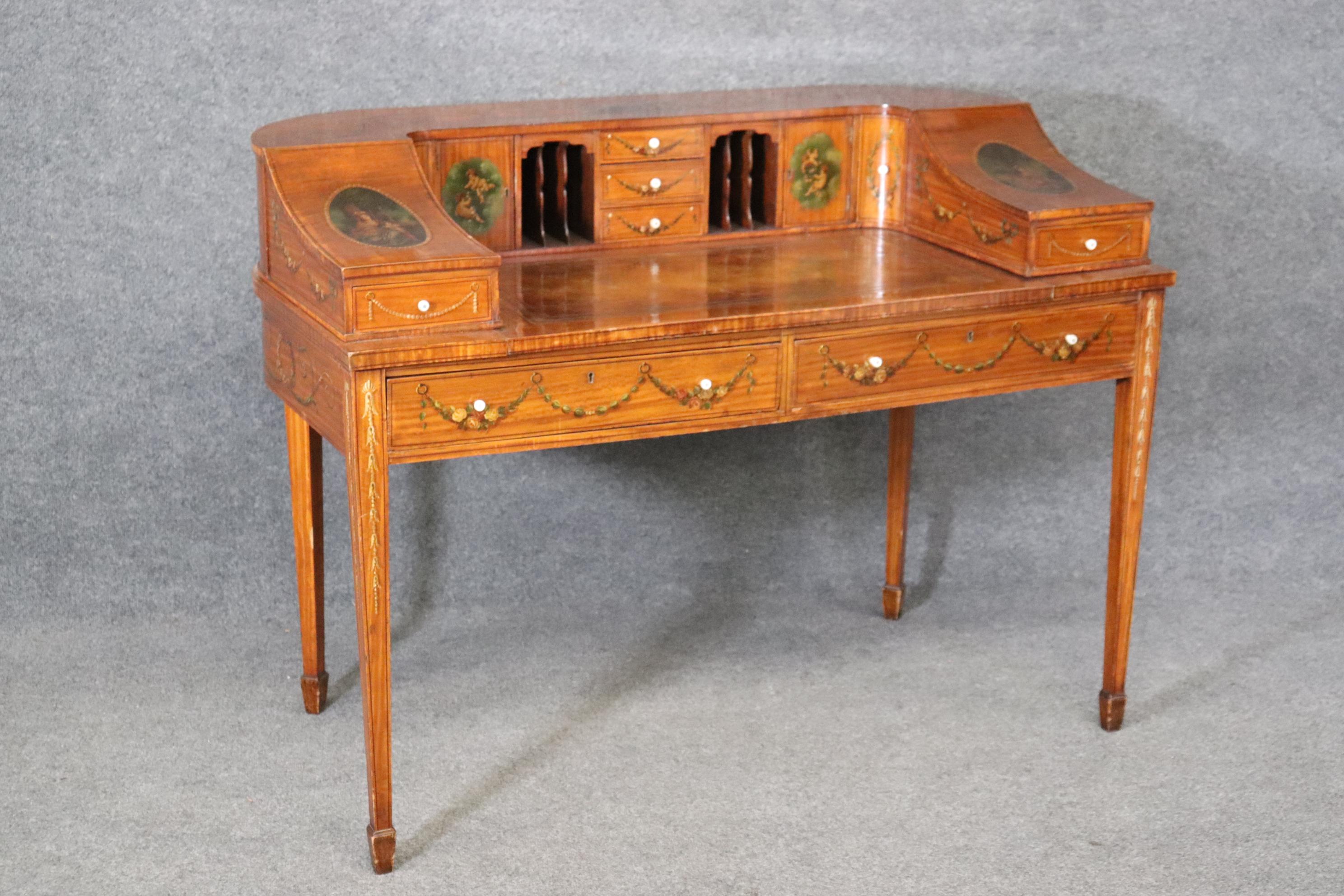 This is a spectacular hand-paint decorated satinwood Carlton House desk with beautifully painted cherubs and musical instruments, flowers and figures. The desk is in its original finish with some signs of age and use including minor losses to the