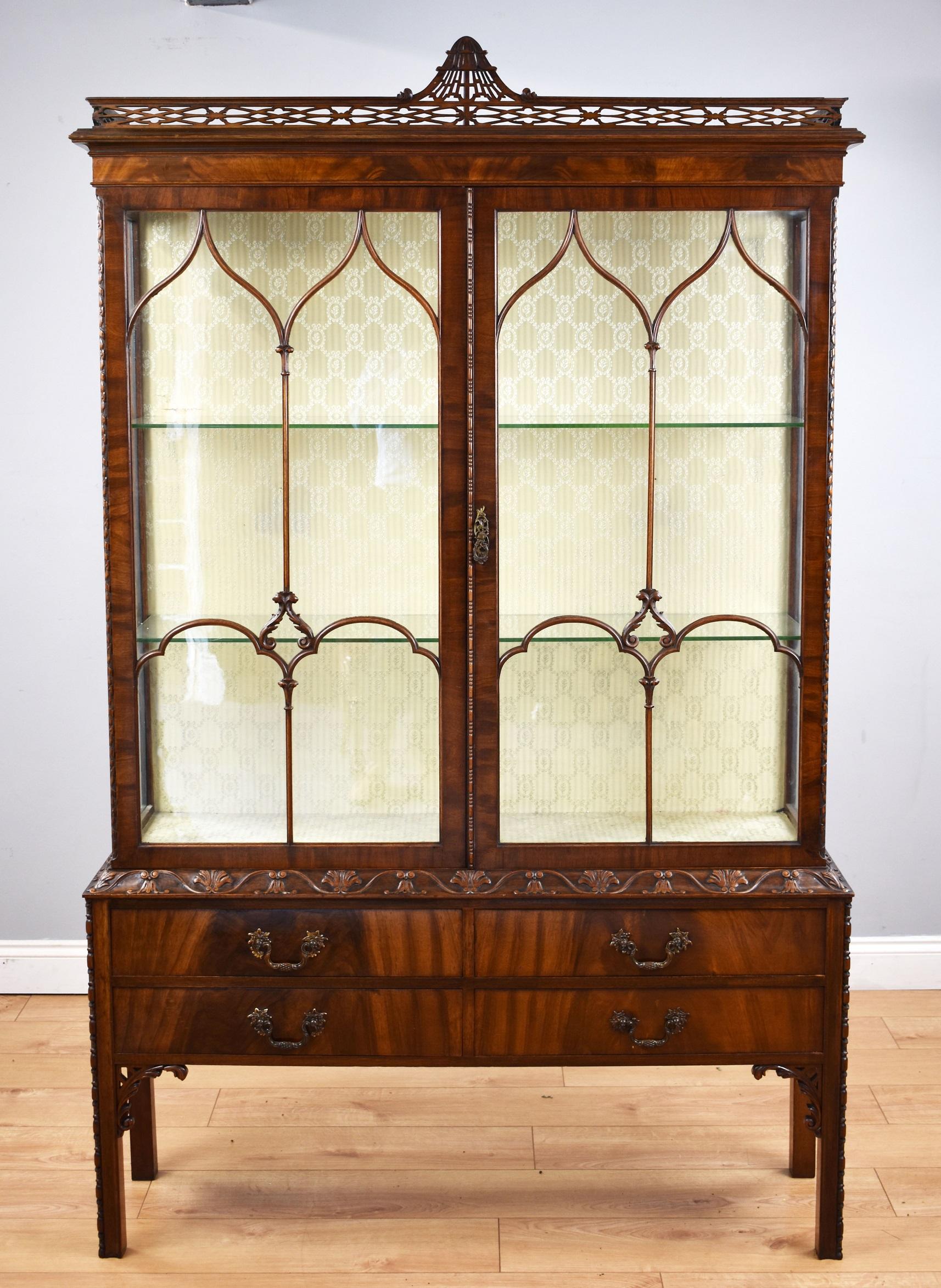 Fine quality flamed mahogany Chinese Chippendale style display cabinet in good condition, the top has decorative open fret work with two astragal glazed doors enclosing two glass shelves. The base has decorative edges with four drawers and stands on