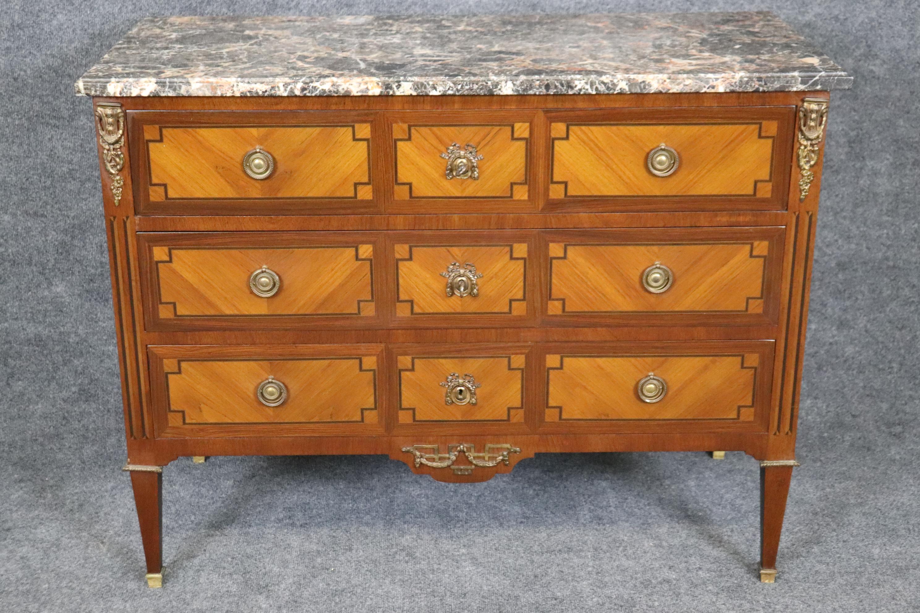 This is a beautiful commode in the Directoire style or Louis XVI style. The commode features kingwood and walnut in contrasting hues and beautiful bronze. The piece features a beautiful marble top and is in good antique condition with minor signs of