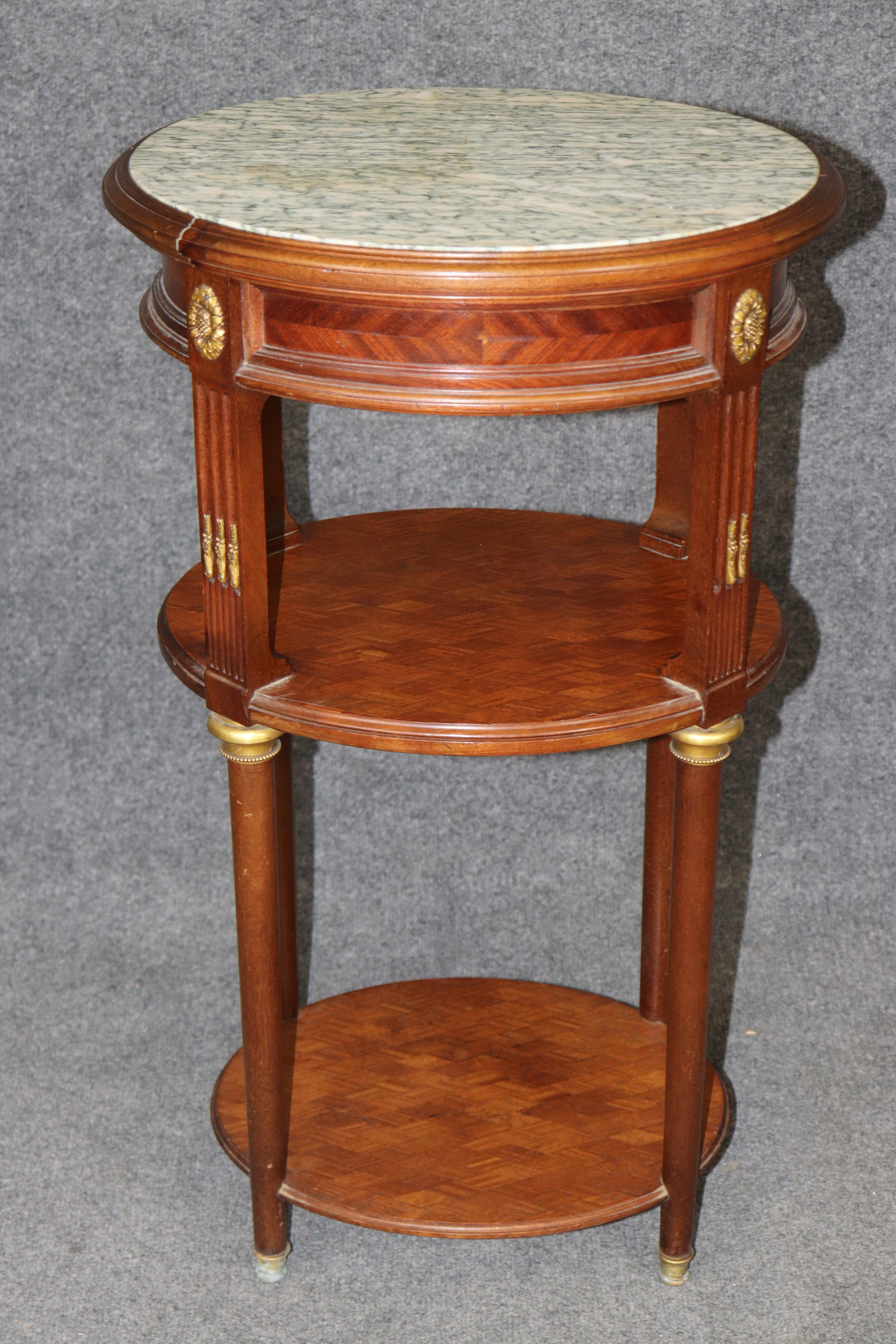 Mesa Luis XVI de tres pisos con pedestal y tapa de mármol - Montada en bronce, estantes de parquet - Atribuida a Henri Picard

Este magnífico pedestal o mesa auxiliar de tres niveles de estilo Luis XVI es una pieza de rica factura atribuida al