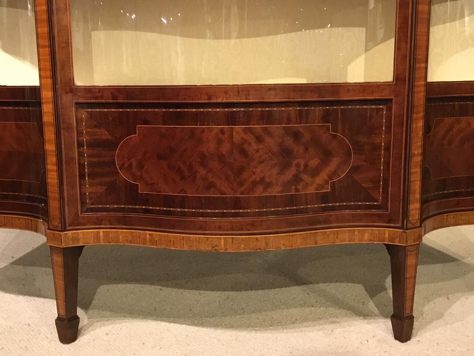 A fine quality mahogany inlaid Edwardian Period serpentine display cabinet by Maple & Co. Of serpentine outline throughout, having a moulded cornice above a flamed mahogany and mahogany inlaid frieze and chequer band inlaid border. The central