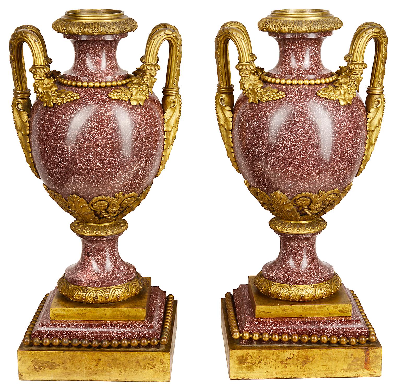 A fine quality pair of neoclassical 19th century French vibrantly coloured Porphery urns, each with wonderful gilded ormolu mounts and handles of scrolling foliate and grapevine decoration, raised on plinth Porphery and ormolu bases. Measures: 56cm