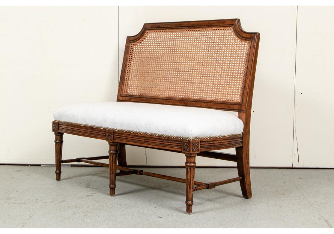 Very well made and comfortable pair of cane back upholstered seat benches. The pair feature fruitwood stain frames with well carved legs and stretcher base. 
The seats are upholstered in soft plush white velvet and have brass nail-head trim.