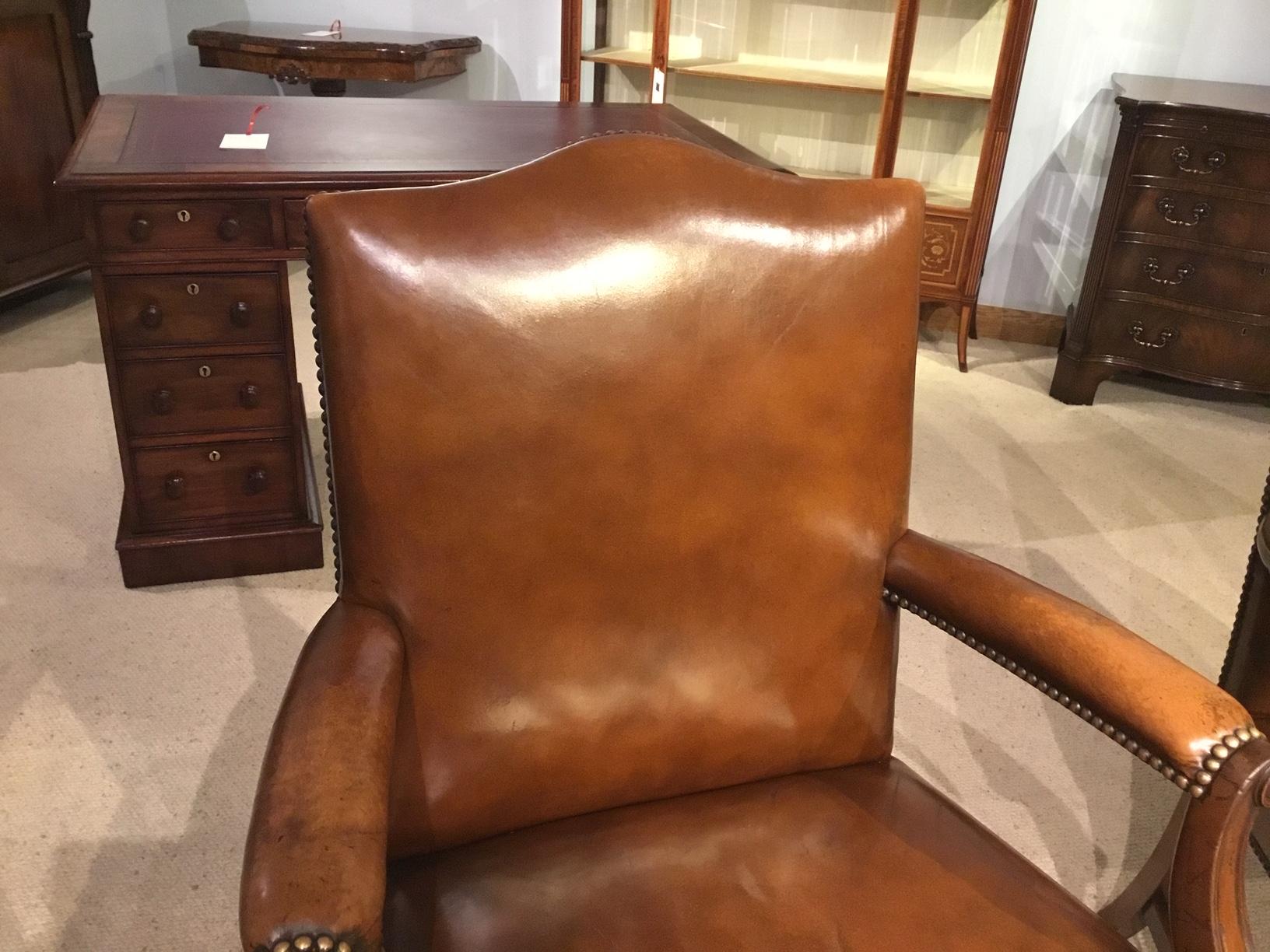 A fine quality pair of mahogany Gainsborough armchairs upholstered in tan leather. Each having a shaped padded back, padded open arms with shaped supports and turned mahogany roundels. Having generous shaped seats with close nail brass stud detail,