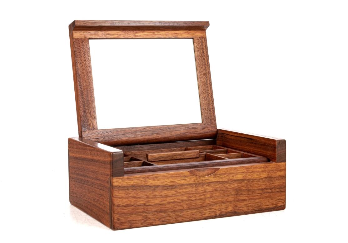 Boîte à bijoux en bois finement ouvragée avec couvercle en laiton et doublure en miroir. La boîte est munie d'un plateau amovible divisé, compartimenté et doublé de tissu qui révèle un espace de rangement supplémentaire doublé en dessous.
Le coffret