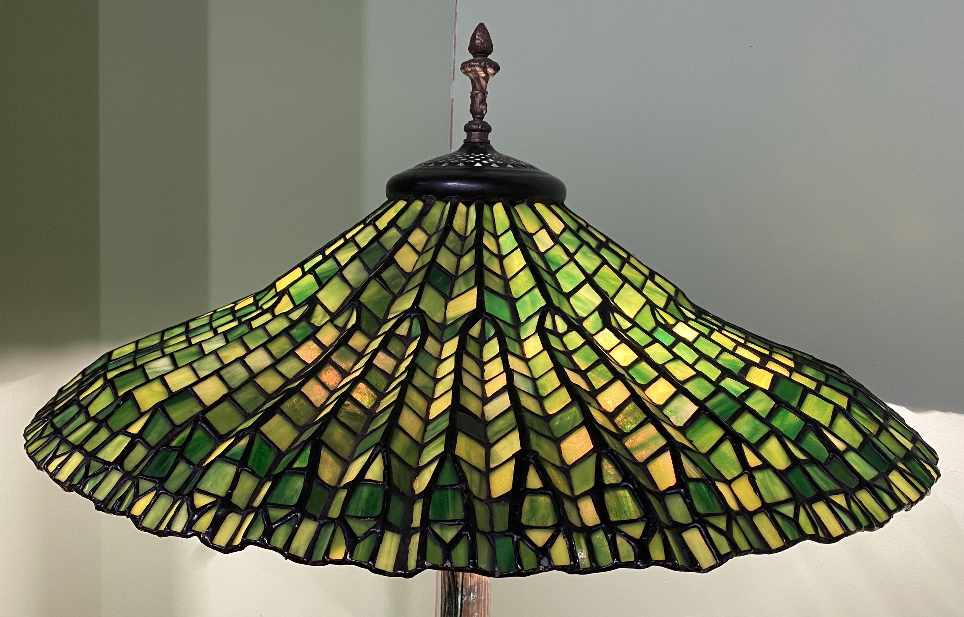 A fine quality Tiffany Studios style Lotus leaded glass four light floor lamp with varying shades of green tiles in the shade, with hints of orange and yellow,  mounted on a brown patinated tree form metal base with verdigris. The lamp dates to the