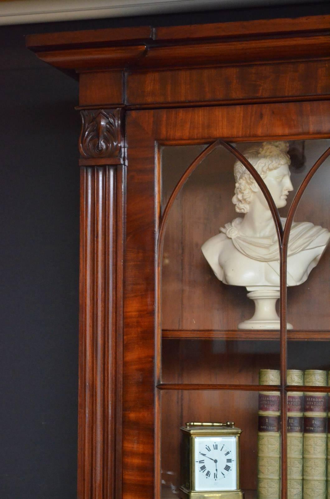Sn4307, handsome William IV bookcase in mahogany, having moulded cornice above a pair of astragal glazed doors fitted with original working lock and a key and enclosing three height adjustable shelves, all flanked by fluted columns with carved