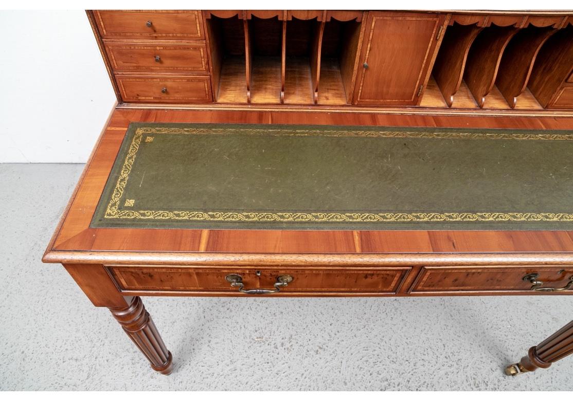 A well-made and handsome Writing Table in Banded Yew Wood. The elevated back section with small banded drawers flanking the cubby holes with carved frames, and a center banded door. The writing surface with carved bull nose edge and green tooled