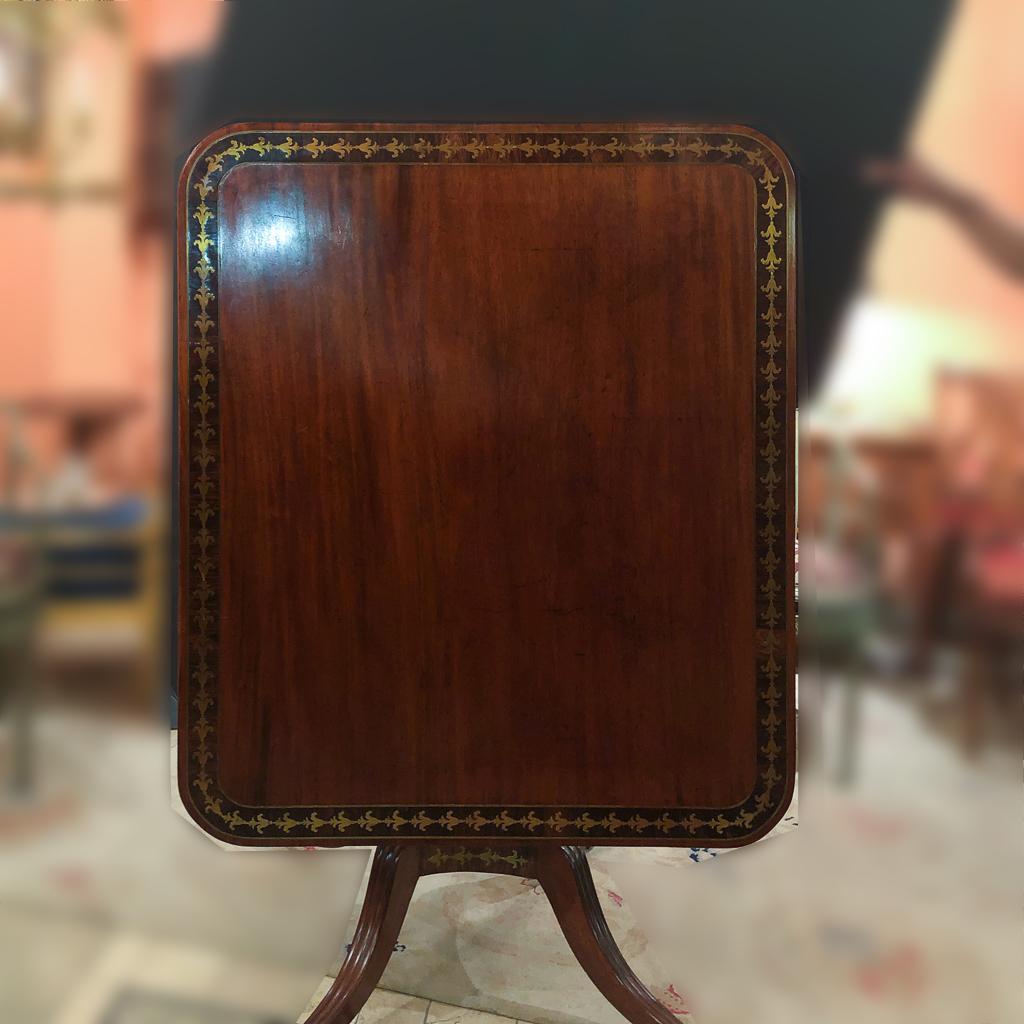 A fine English Regency mahogany tilt-top breakfast table with brass inlaid Calamander crossbanding, four column pedestal support on a brass inlaid base with brass caster feet.
