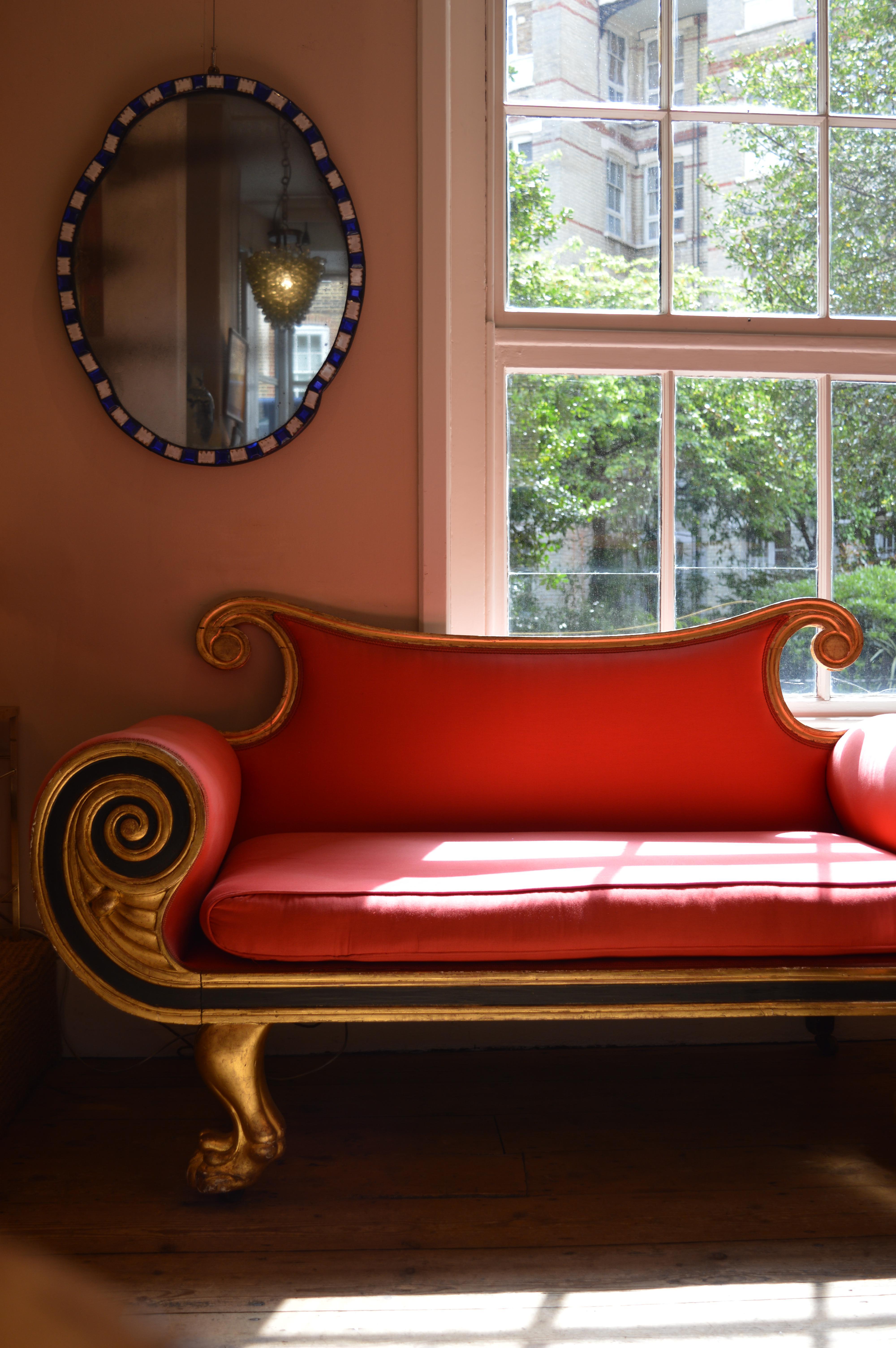A fine early 19th century daybed with scrolled back rails and exaggerated circular armrests, supported on boldly carved hairy paw feet. Upholstered in a vivid red fabric.
