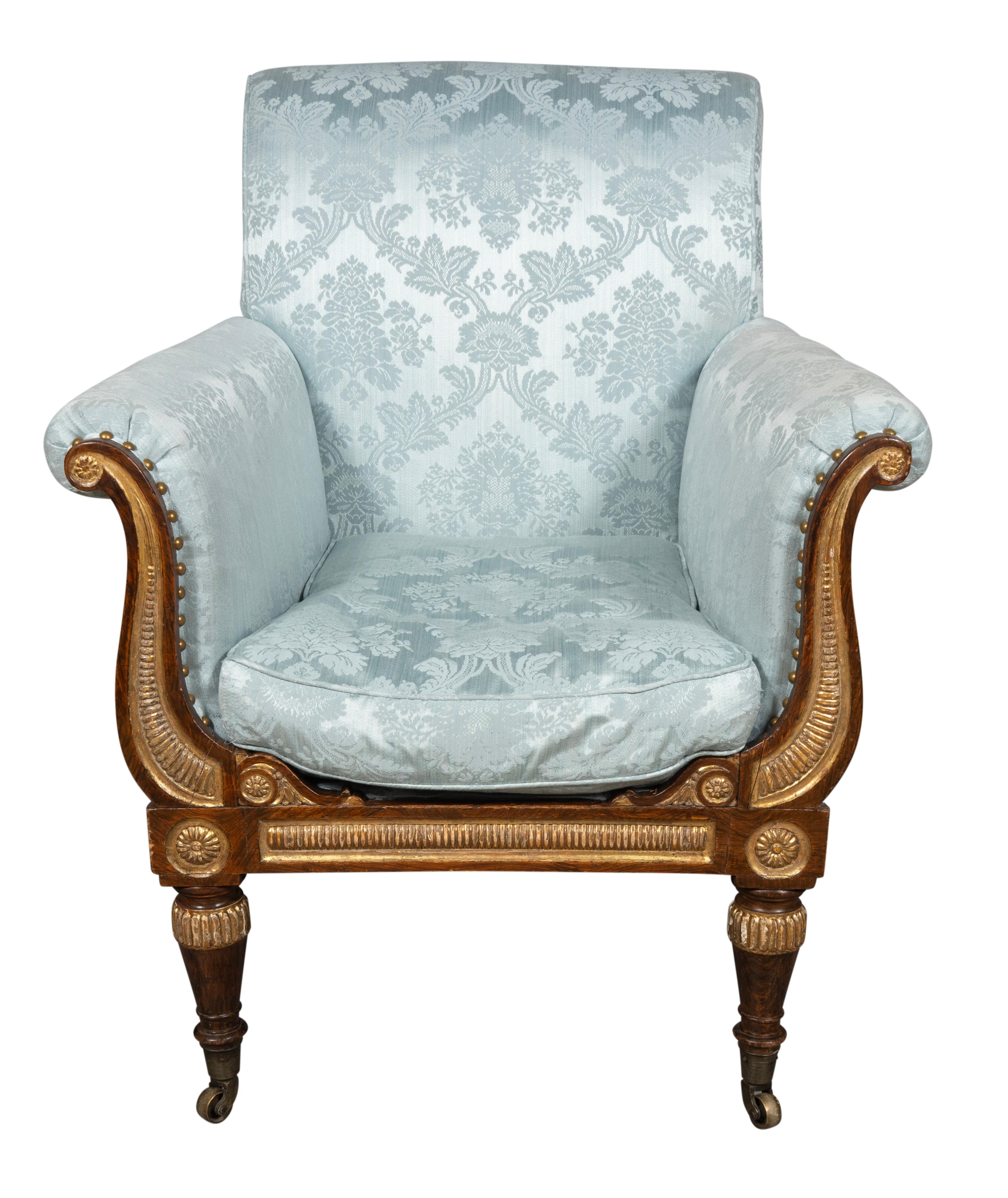 Fauteuil très confortable avec assise profonde, dossier en volute et accoudoirs à volutes recouverts de damas bleu. L'avant des bras est orné de détails dorés et sculptés. Les pattes circulaires effilées sont dirigées par des paterae. Roulettes.
