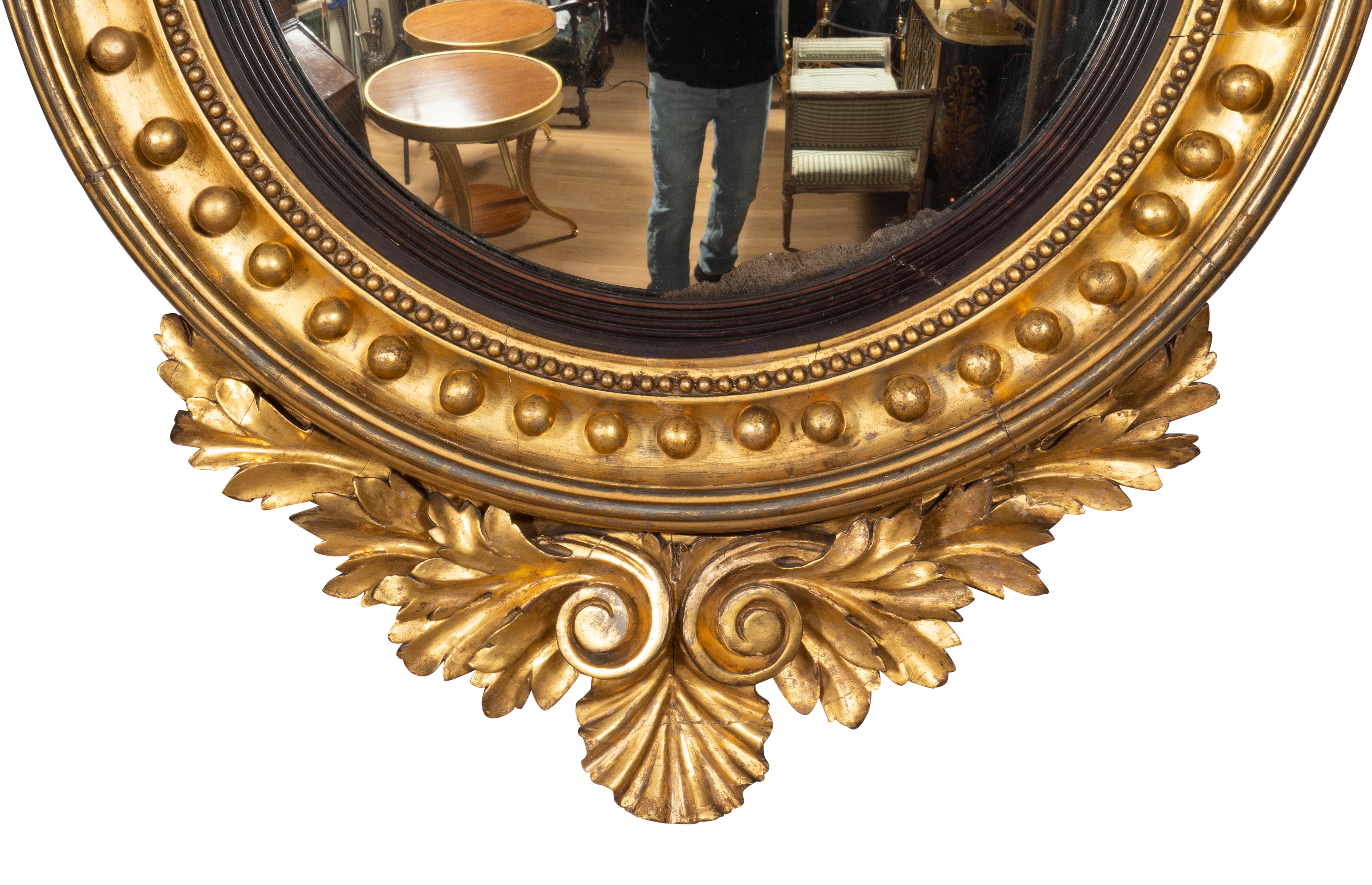 With convex glass and ebonized band in a conforming frame with mini spherules all around, flanked by acanthus leaves and headed by an eagle standing on a conch shell. The base of the mirror with acanthus leaf carved decoration. Original gilding with