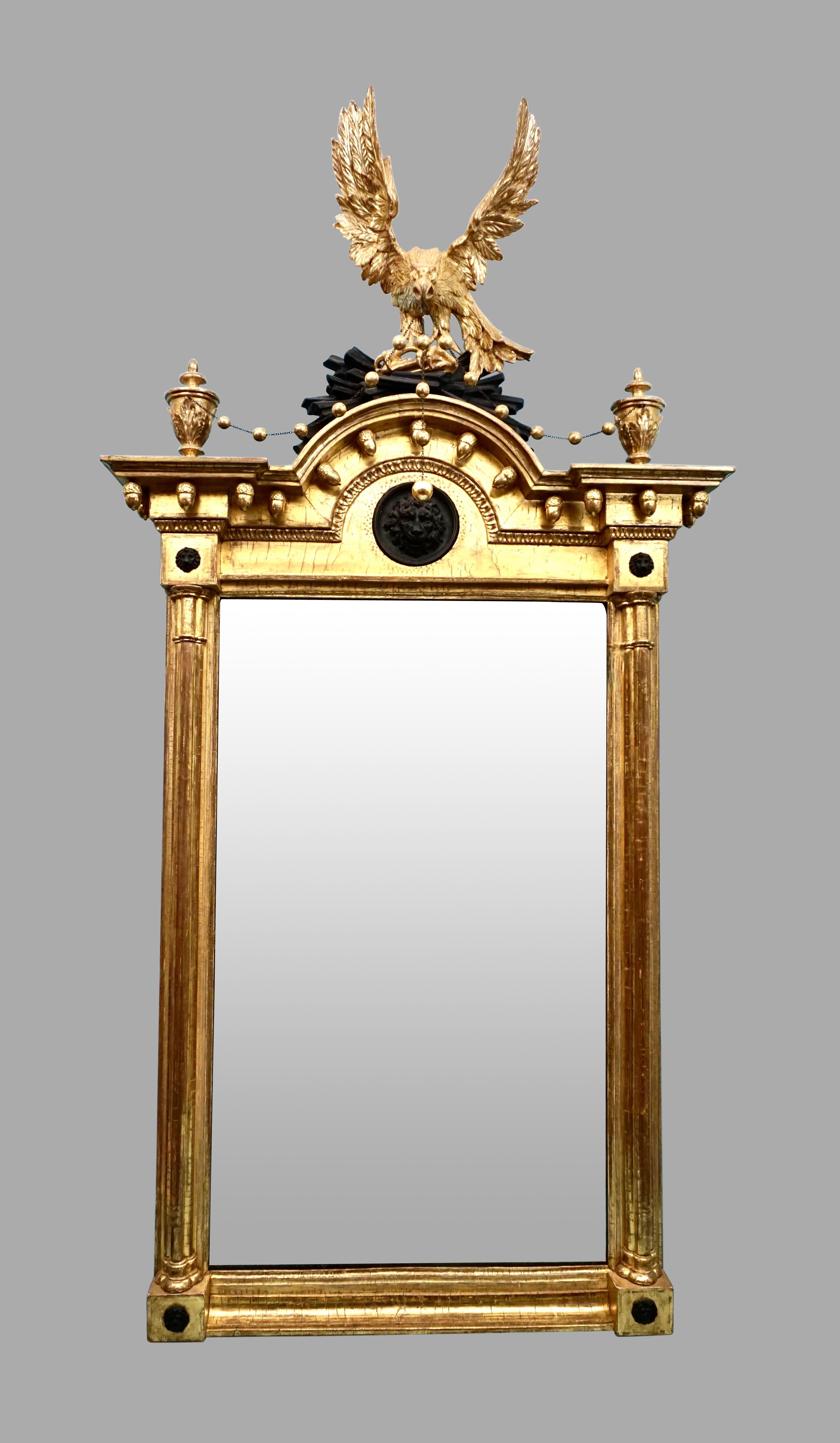 A superb quality English Regency period pier mirror, the replaced mirror plate surmounted by a beautifully carved eagle with spread wings and a downward gaze atop a demilune cresting centered with an ebonized lion mask. The eagle holds a delicate
