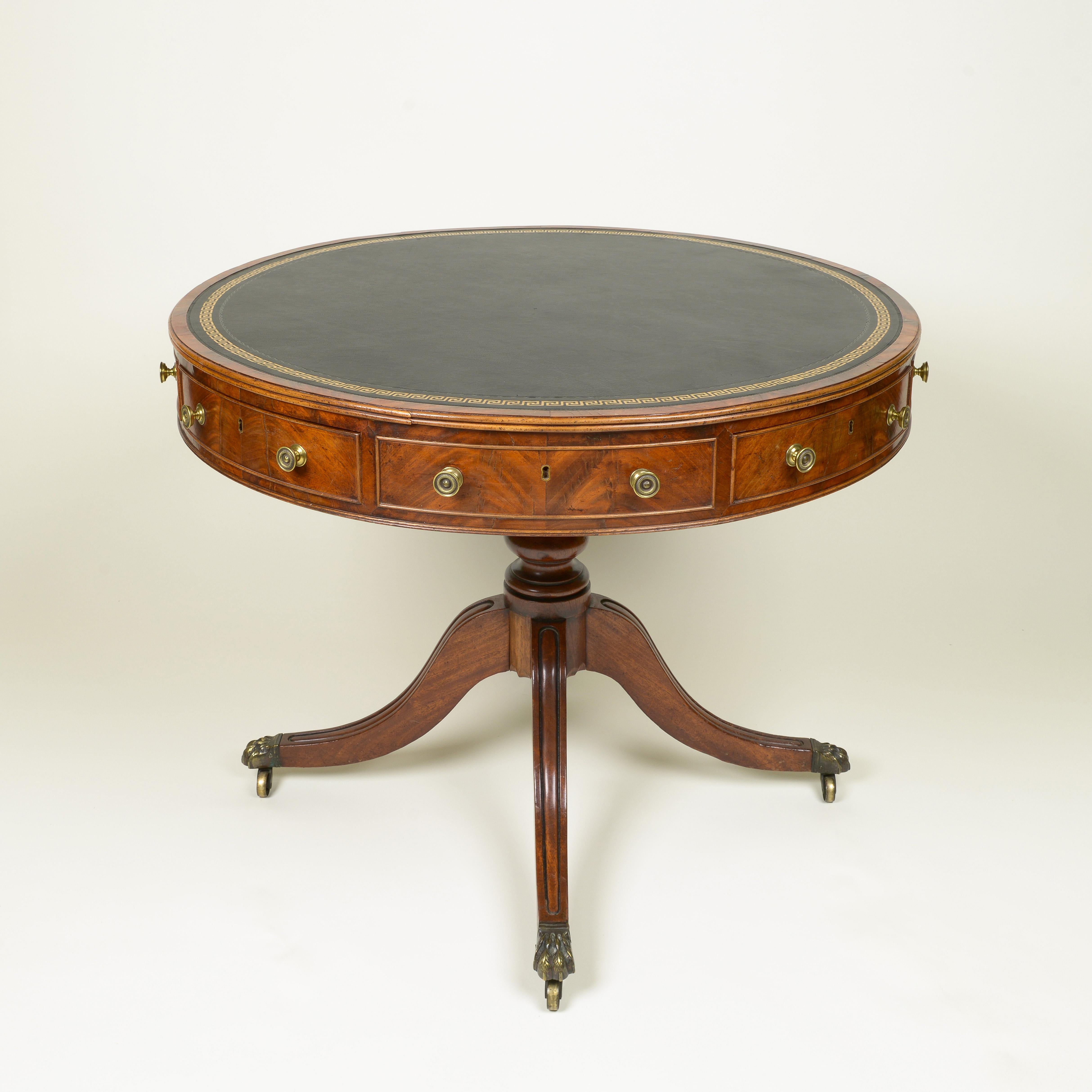 Black leather-lined top embossed with gilt greek key border over a reeded edge and frieze fitted with drawers veneered with vibrant book matched mahogany, raised on a turned pedestal support issuing four channeled legs and terminating in brass feet