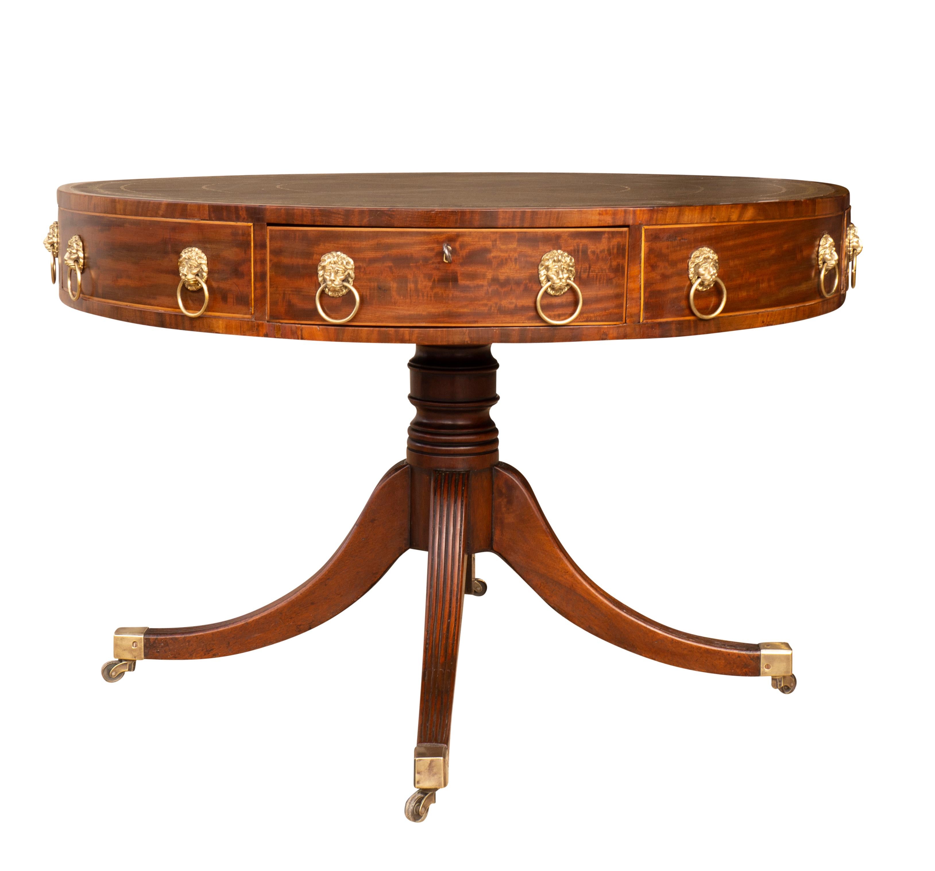 With a new circular green tooled leather top within a banded edge over conforming frieze with  alternating false and working drawers all with lions head drawer pulls, the elegantly proportioned base with turned support and four reeded saber legs