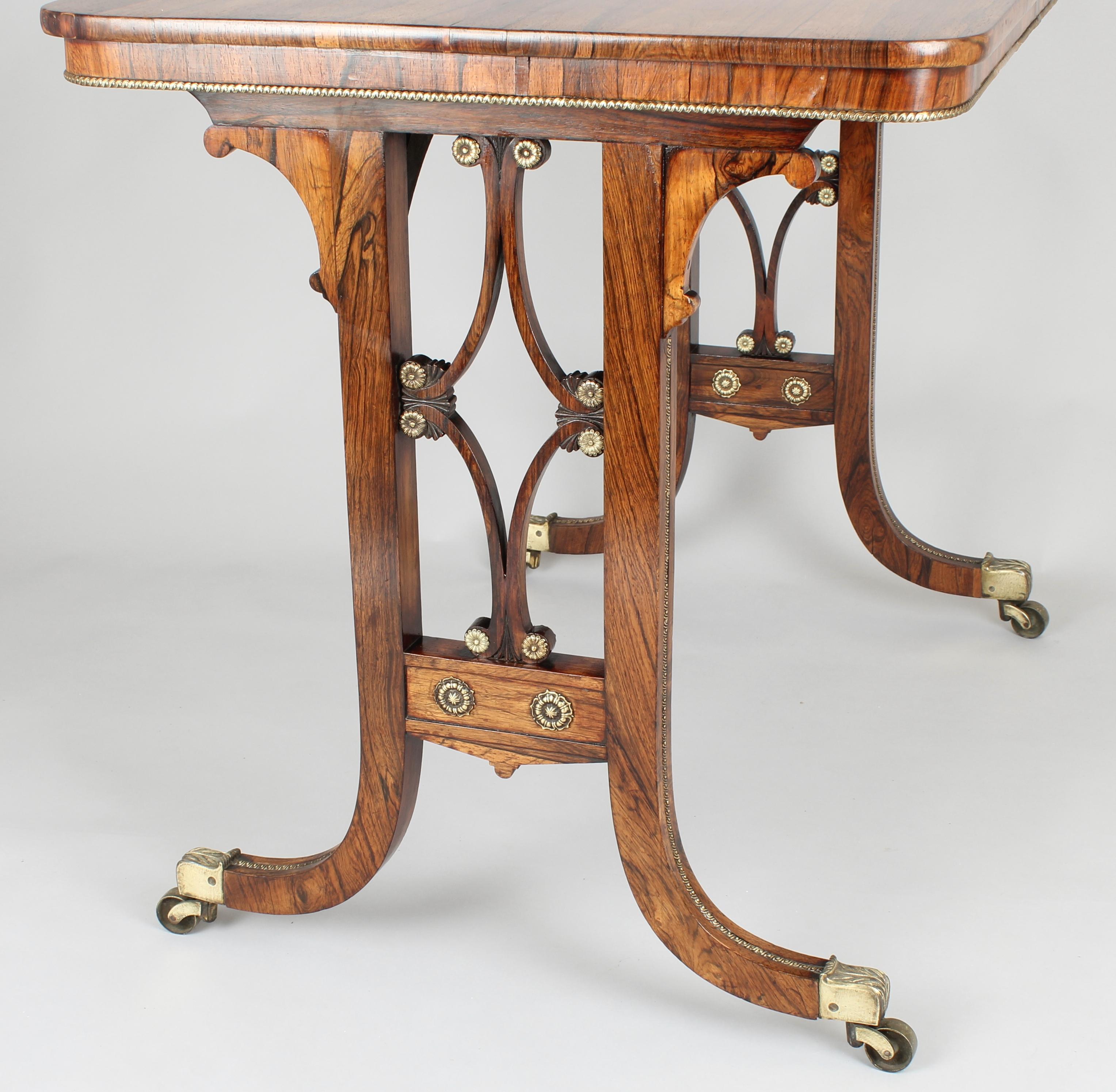 Fine Regency period rosewood end-standard centre-table of finely-figured timber; the top with rounded corners and an applied brass beaded border; on 'hockey-stick' legs with openwork scrollwork panels, applied with brass paterae, brass moldings and