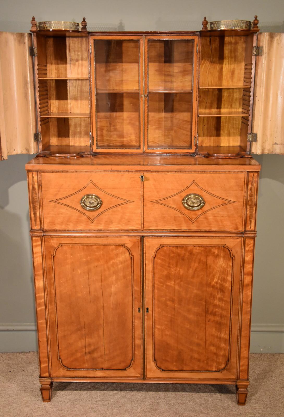 An early 19th century Secretaire cabinet in the manner of George Oakley, the upper gilt metal gallery over a pair of glazed cabinet doors flanked by barrel form cabinet doors enclosing adjustable shelves. The Secretaire cabinet is fitted with solid