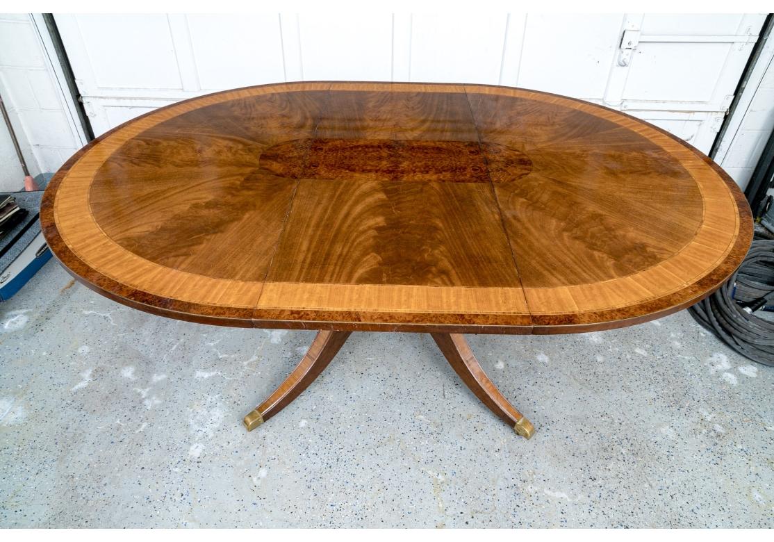 English round mahogany pedestal dining table with satinwood and yew wood banding and yew wood burl center inlay.  Raised on a central birdcage form pedestal with four carved saber legs with brass toe caps and casters. 
Reproduction, purchased from