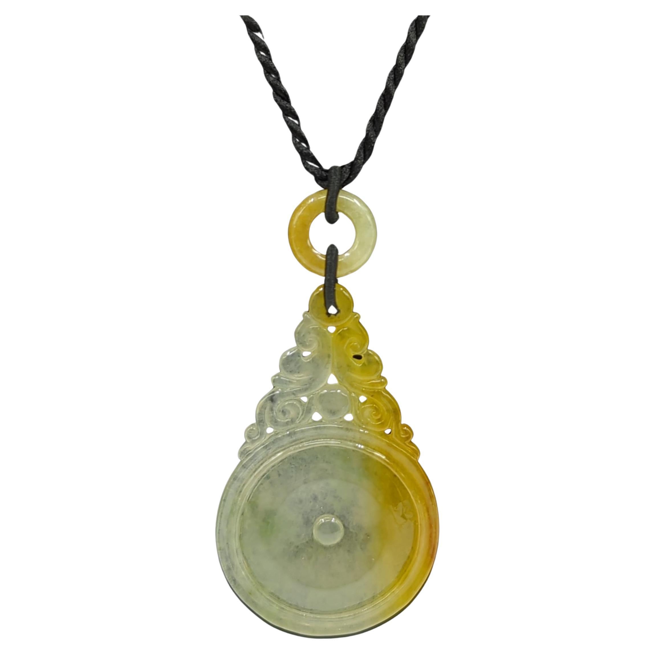 A  finely carved and pierced natural honey yellow jadeite pendant with light moss green inclusions, featuring a circular bi disc medallion, topped with scrolling foliage and linked to a circular yellow jadeite bead

This fine jadeite necklace makes