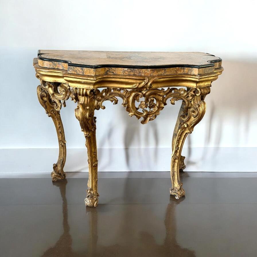 Roman mid-18th century gilt-wood Rococo consoles with a  Yellow Siena veneered marble top within a black  marble surround, above a pierced frieze centered by a foliate cartouche, on cabriole legs with scrolling acanthus leaves and palmettes on