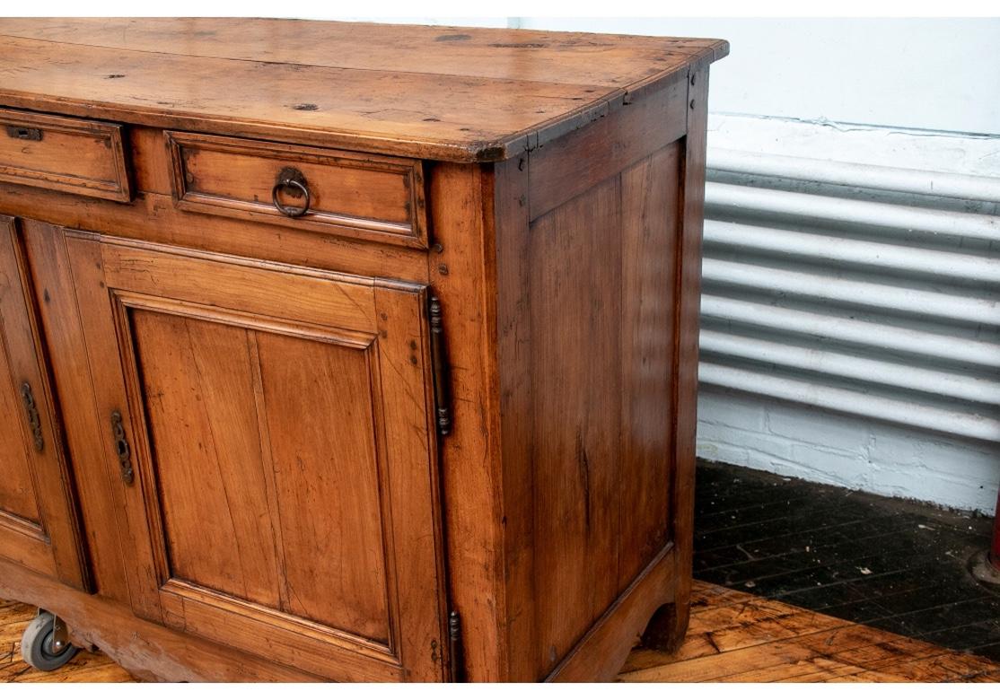A fine antique English cupboard in nicely age colored elm, circa 1850. A plank constructed top with canted front corners over three apron drawers with carved moldings. The center one with an escutcheon and key. The cabinet with two- panel recessed