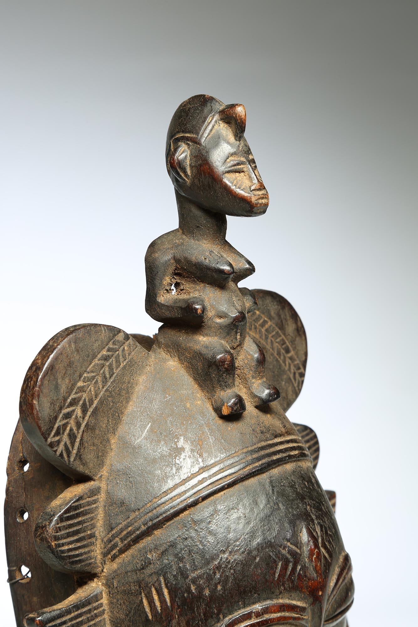 Finely carved and worn Senufo Kepelie dance mask with refined stylized face and small seated female figure on top. Old surface with encrusted patina, worn areas, eye shaped scarification marks below carved eyes and small vertical lip plug. On custom