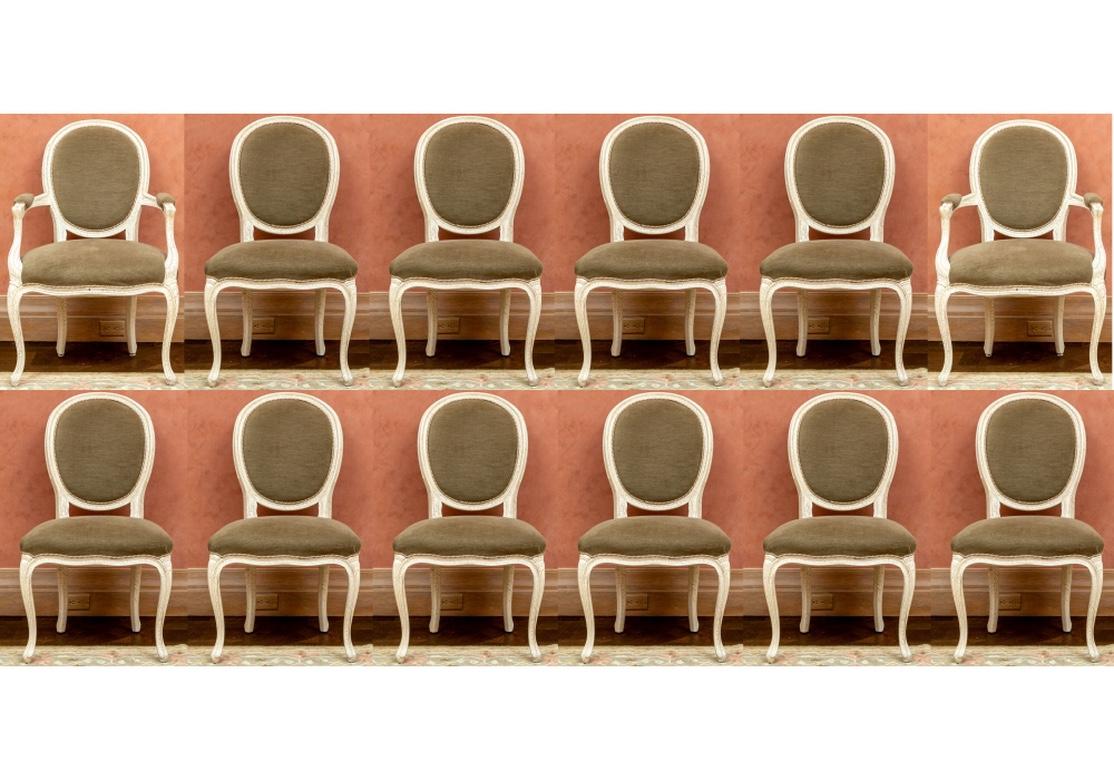 Set of 12 custom dining room chairs comprised of 10 side chairs and 2 arm chairs. The frames were purchased in France and the customer upholstery was done in the States. The chairs in a paint decorated crackle glaze finish with intentional
