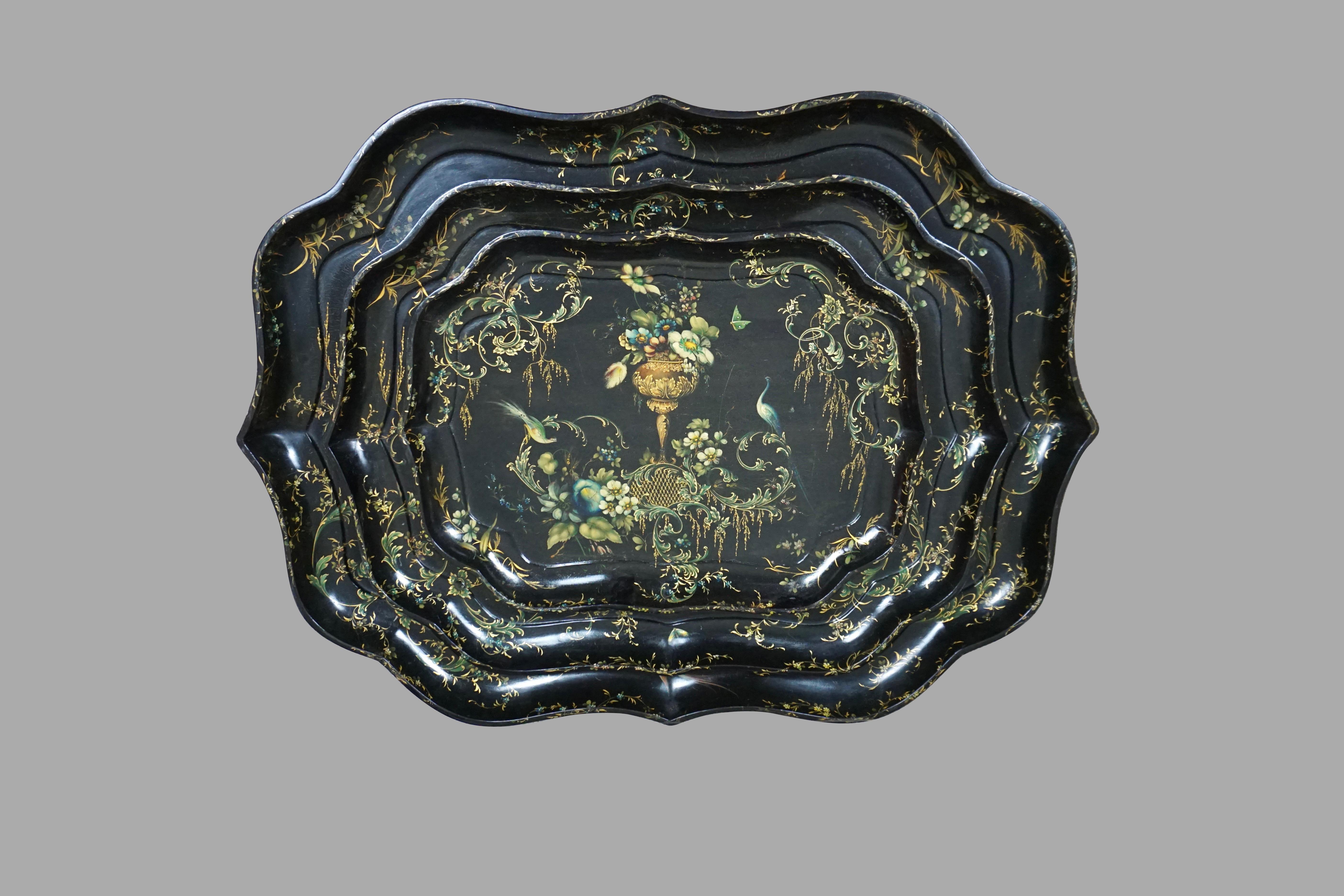 A rare set of 3 English gilt and paint decorated papier mâché scallop form trays with foliate and bird decoration on a black field, the central floral bouquets flanked by exotic birds. It is unusual to find complete sets of graduated trays of this