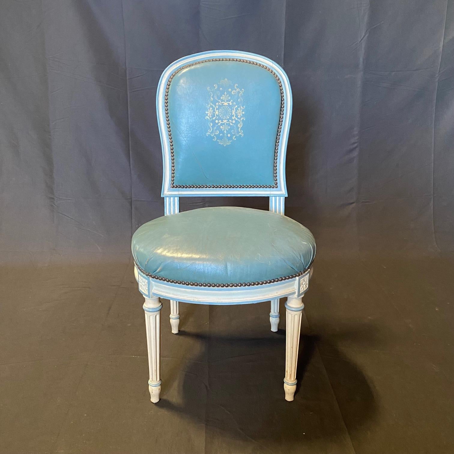 Exquisite and rare unique set of 6 French Louis XVI dining chairs in an antique white painted finish with blue accents and muted blue leather with gold embossing and brass tacking accents. The embossed leather adds such elegance to these superb
