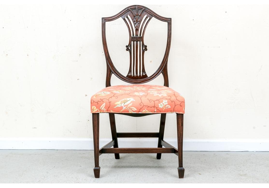 Un set particolarmente raffinato di sedie da pranzo con schienale a scudo in mogano del primo Novecento, con una buona solidità e comodità. Le sedie sono caratterizzate da un covone di grano decorativamente intagliato che sormonta uno schienale