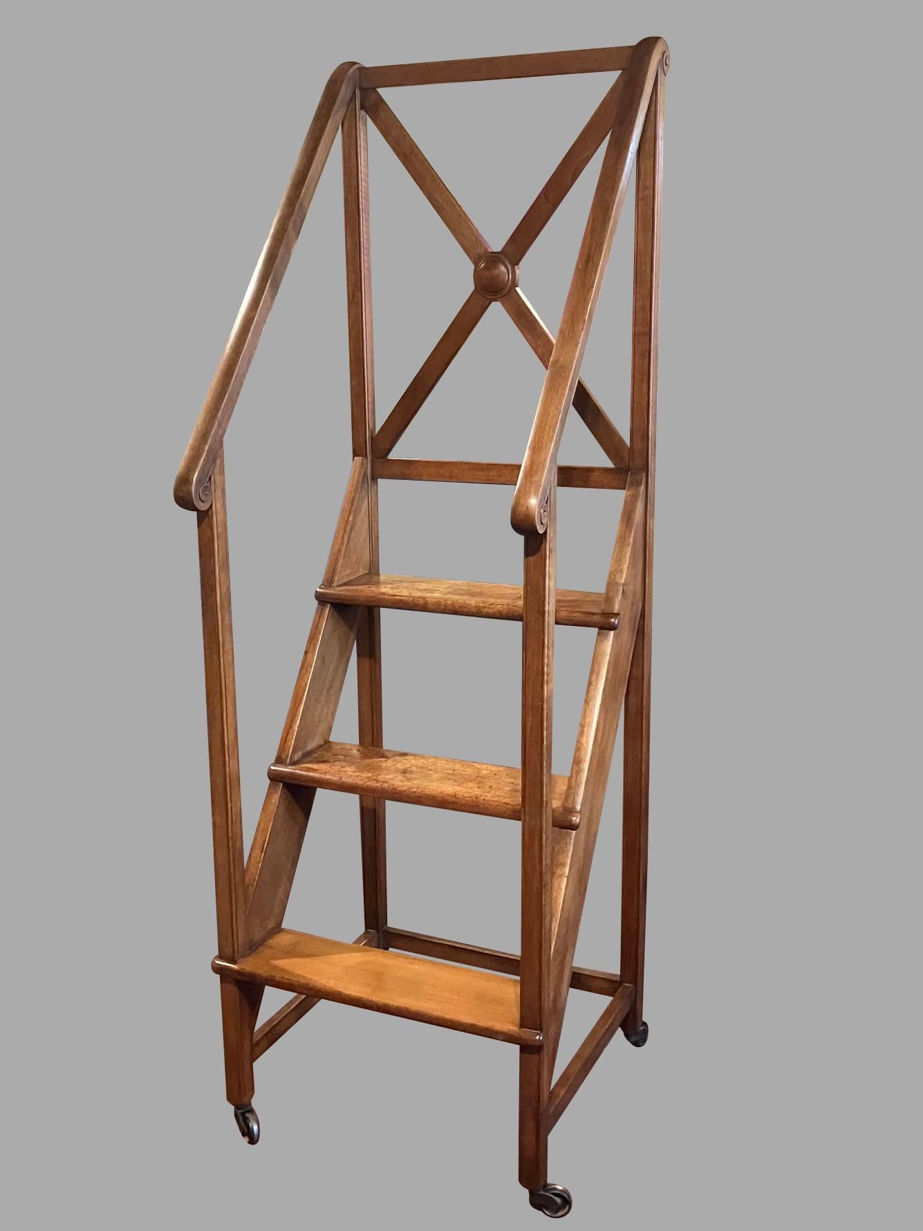 A fine and substantial set of English Regency style library steps with handrails, the 3 treads notched into the frame rising to an X shaped enclosure. The side rails are decorated with turned ends. The steps rest on large steel casters making them