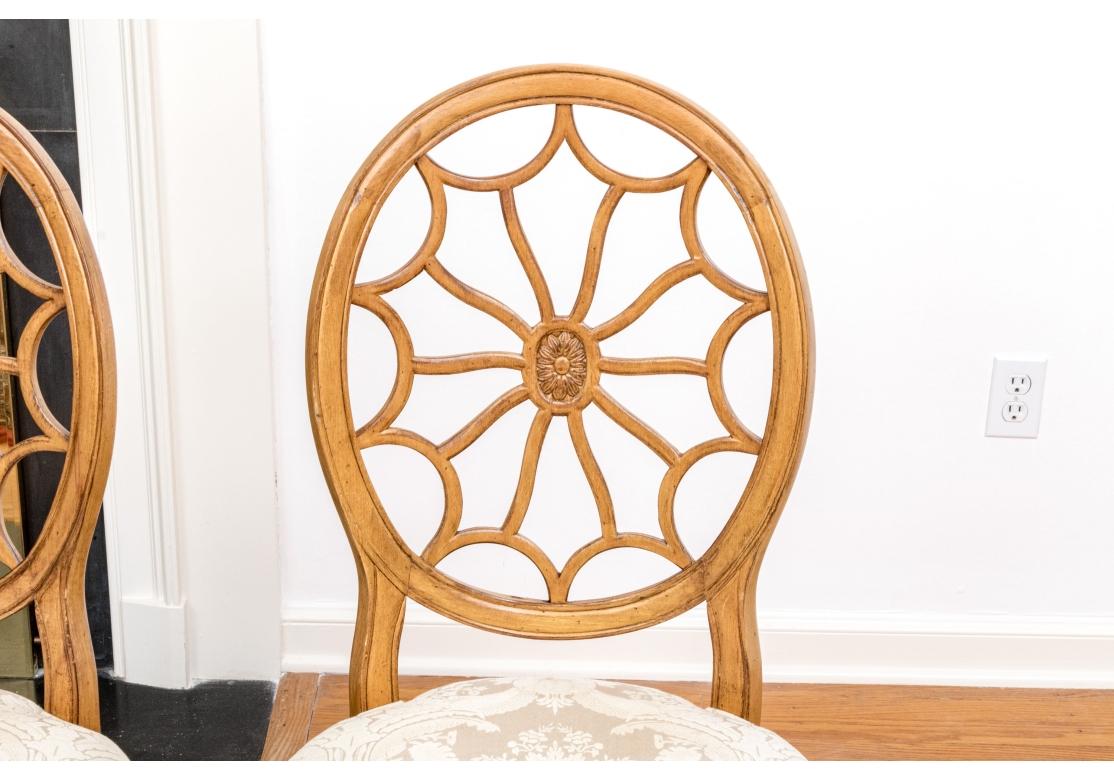 Ensemble de quatre chaises de salle à manger de style Hollywood Regency classique de haute qualité avec dossiers ovales en toile avec le motif classique de toile complexe entourant un fleuron central.   Les châssis des chaises sont joliment finis en