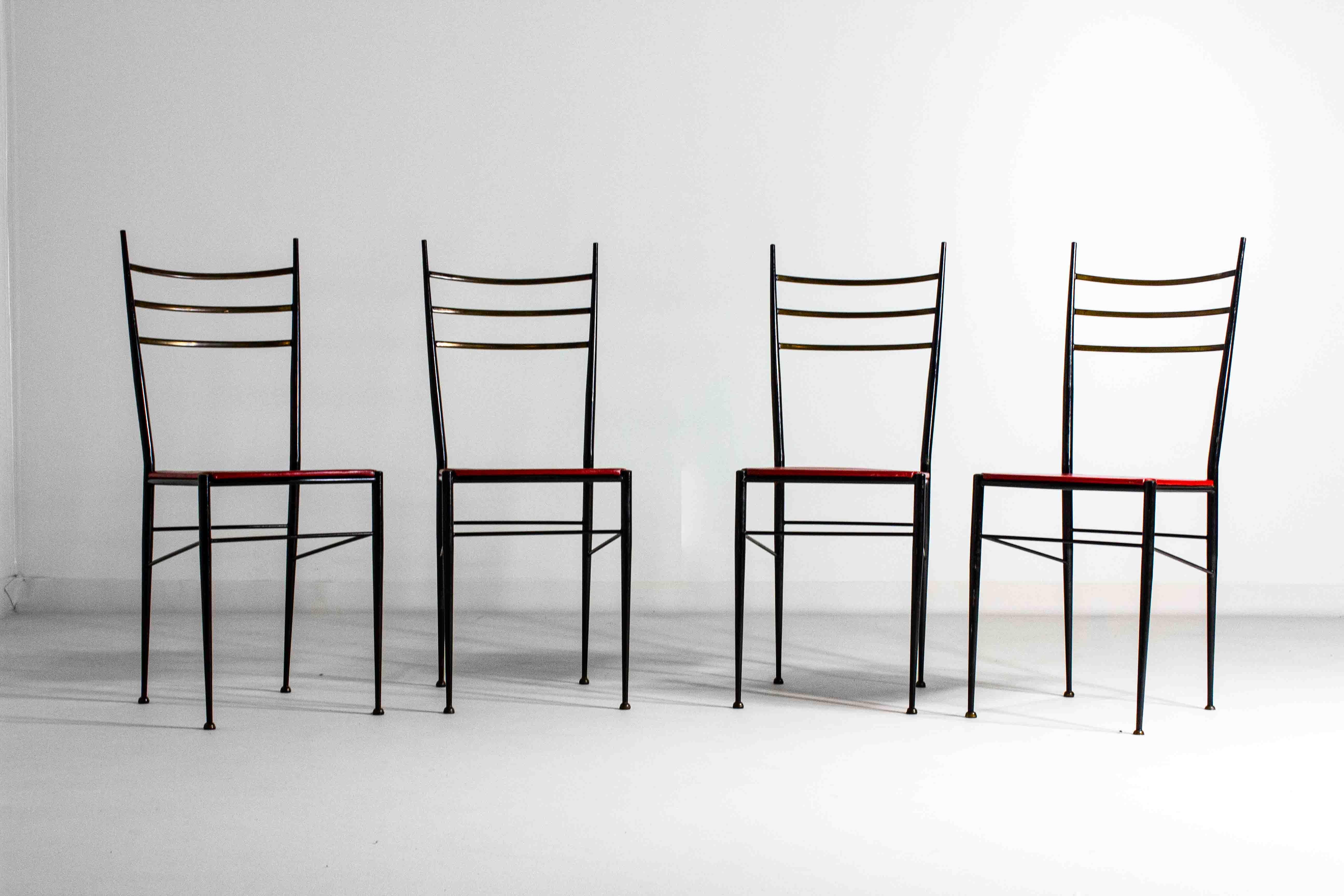 This set of four mid-century modern Italian chairs features black steel frames with brass accents on the backrests. The seats are upholstered in red leather, providing a bold contrast to the dark frames. These chairs combine minimalist design with