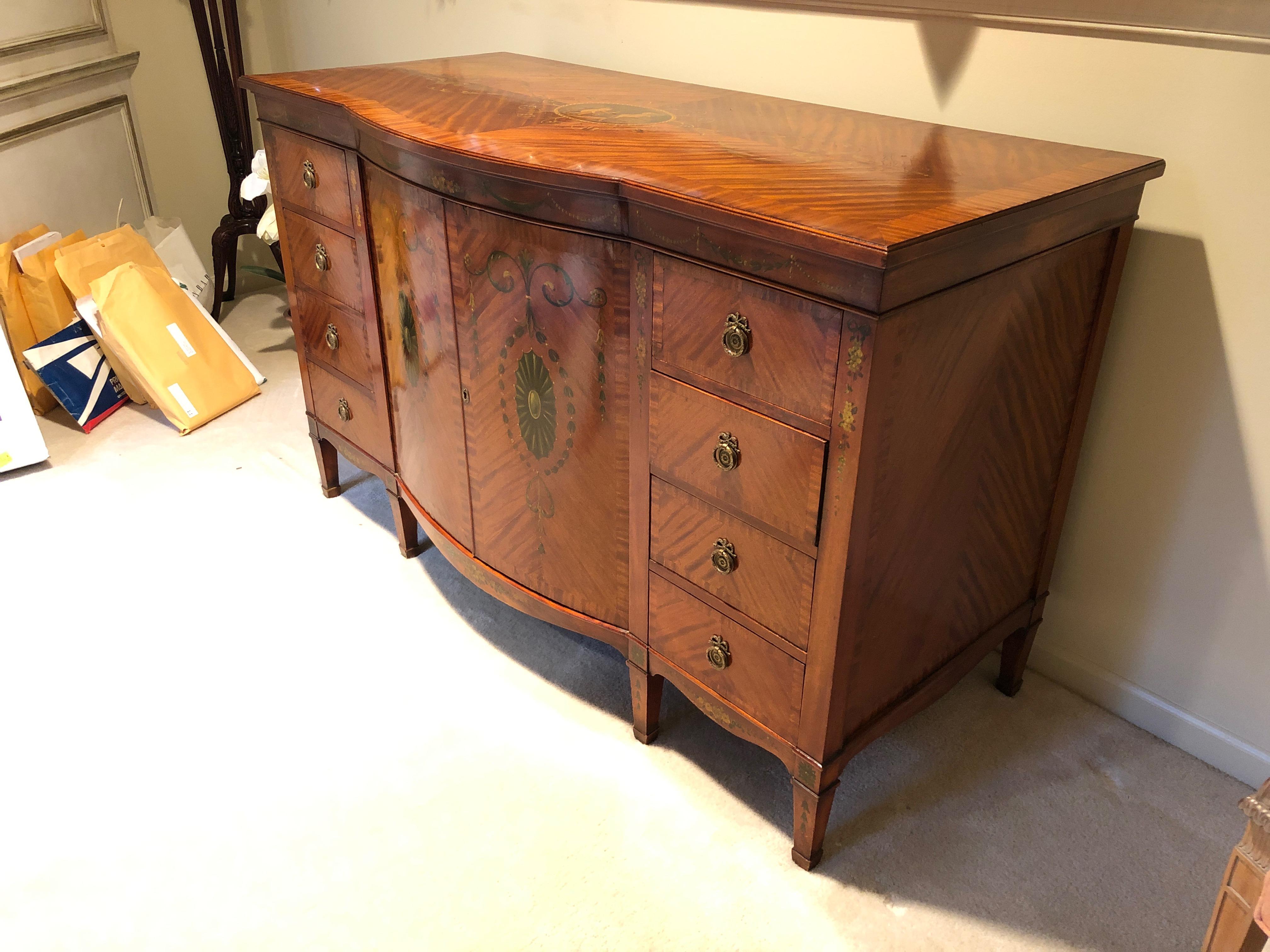 A fine painted satinwood veneer Sheraton Revival sideboard buffet having a frieze and bow front pair of doors painted in Adams style with neoclassical swags, paterae with scrolls and bellflower pendants, having 4 pull out interior drawers or shelves