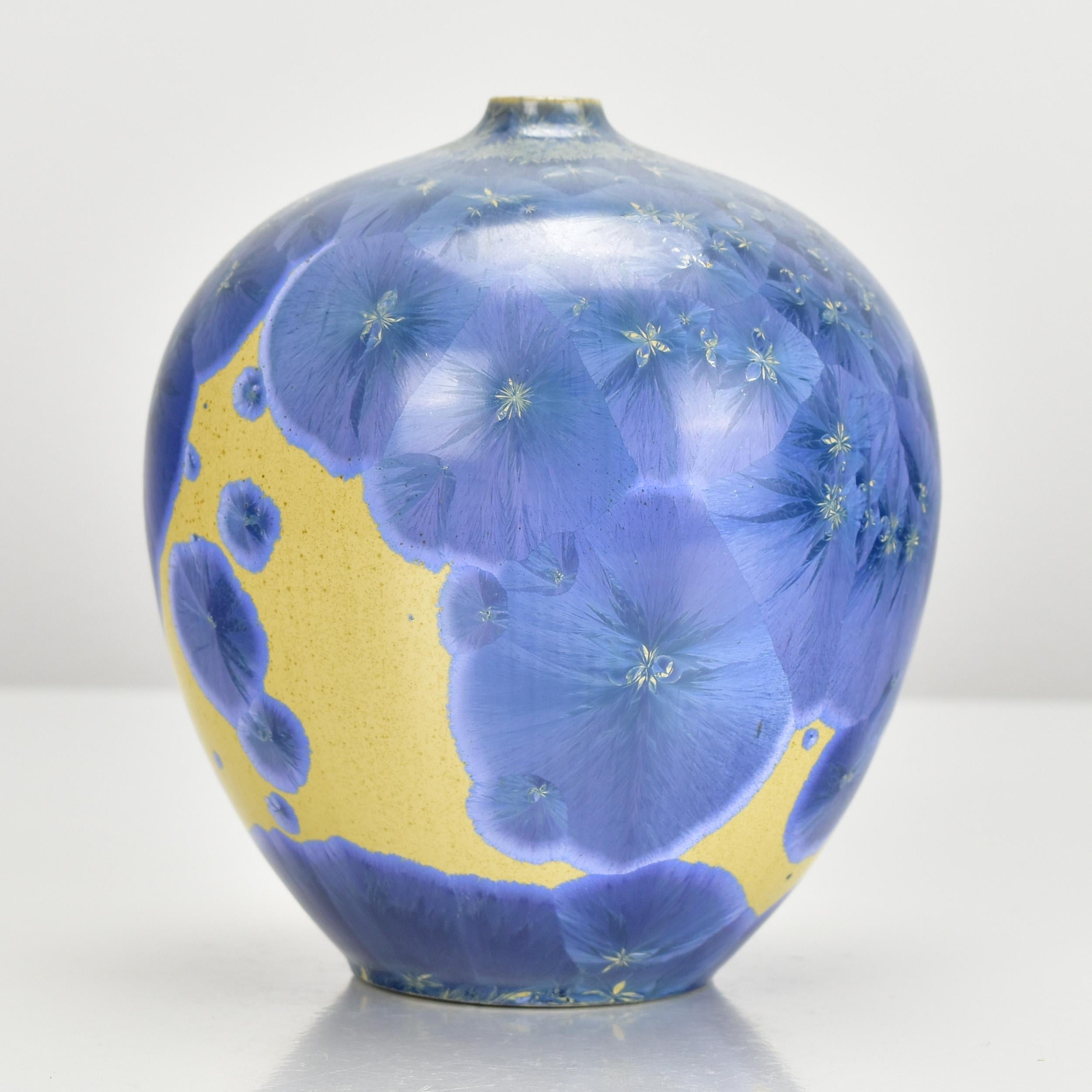A delicate studio ceramic soliflor vase with a blue crystalline glaze on an ocher-colored ground, signed by an unknown artist. The vase exhibits fine craftsmanship and features a beautiful combination of colors, making it an intriguing decorative